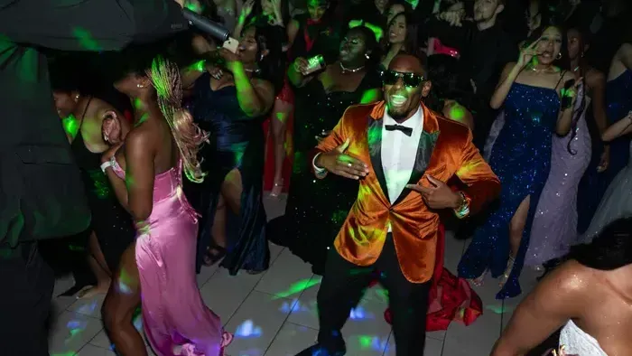 A man in an orange suit is dancing in a crowd of people at a party.