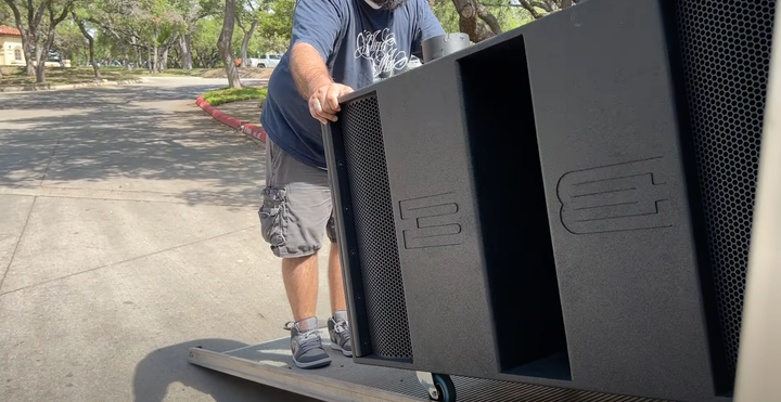 A man is pushing a large speaker on a dolly.