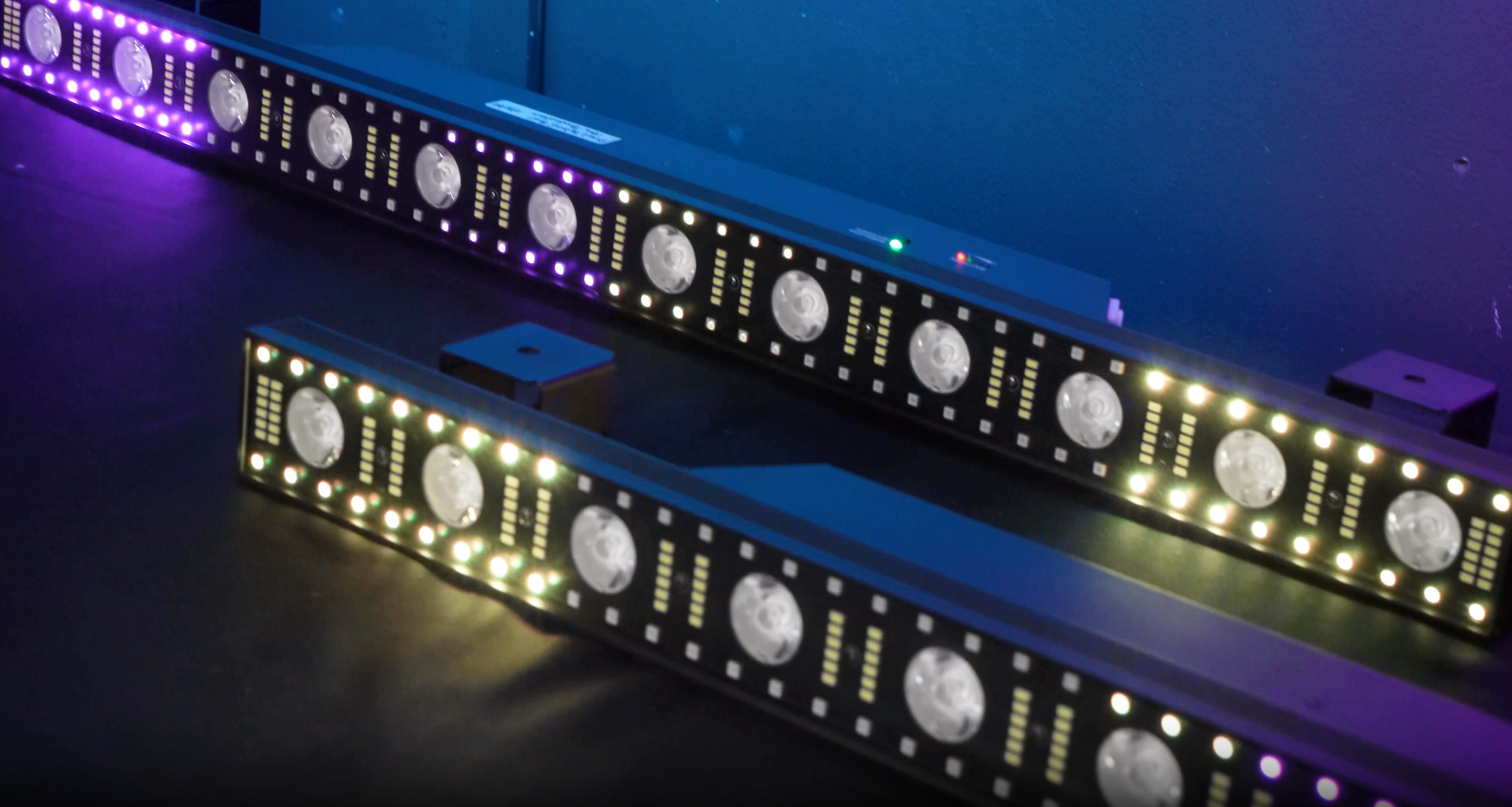 Two RGB LED light bars illuminating with colors on a black surface.