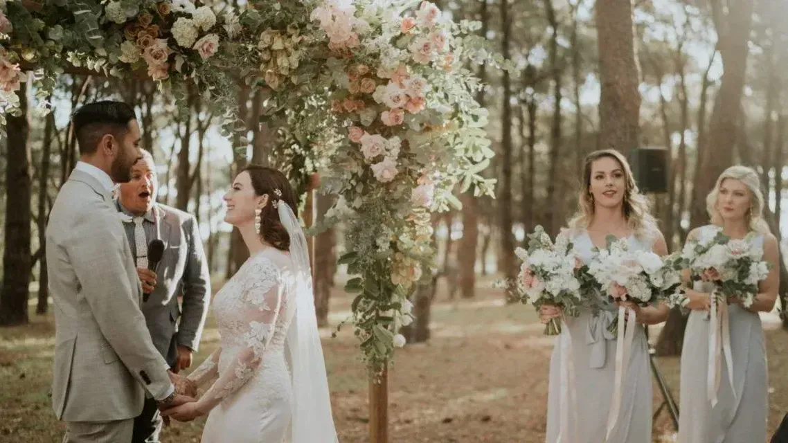 A bride and groom are holding hands during their wedding ceremony in the woods.