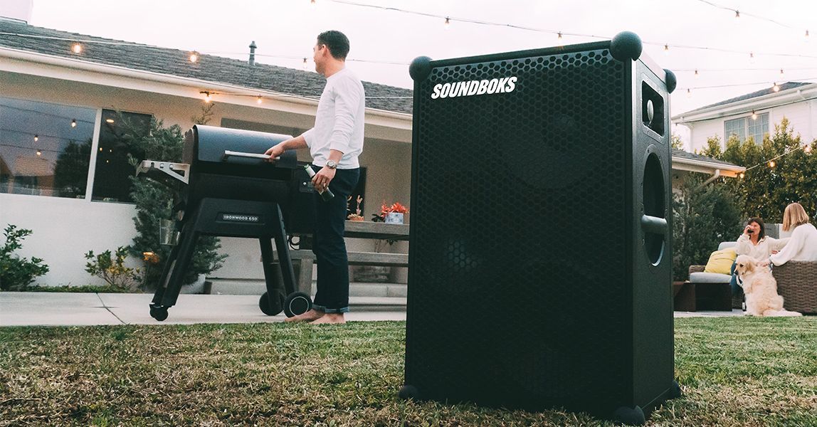 A man is standing next to a Soundboks 3 rental in a backyard.