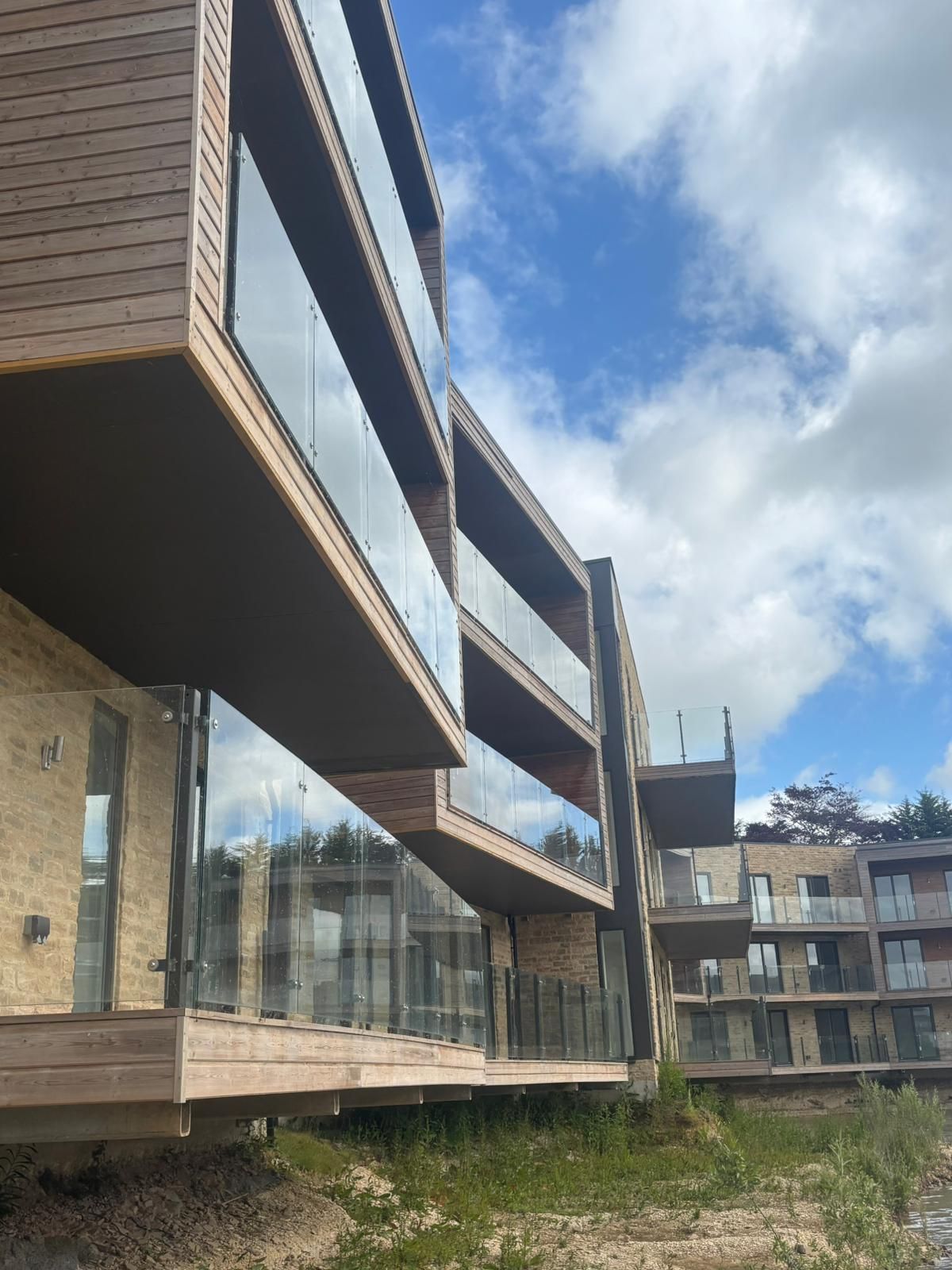 Modern multi-story building with glass balconies and wood siding against a cloudy sky.
