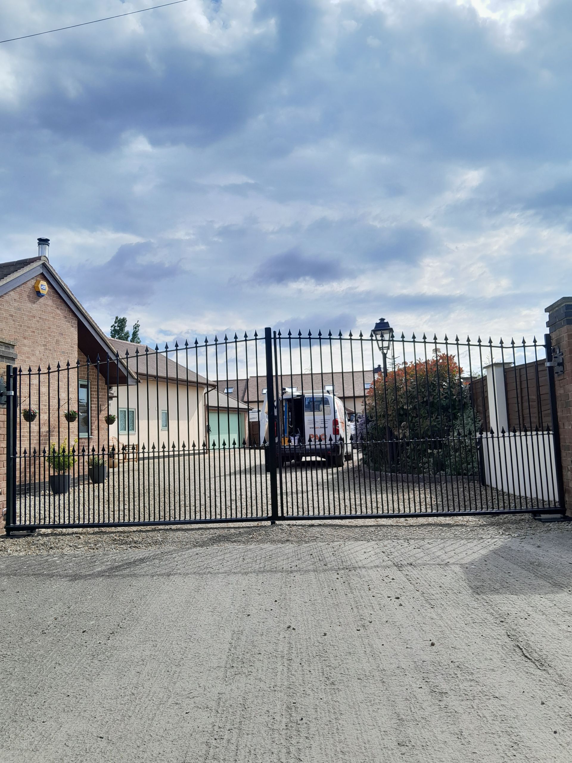 Black wrought iron gate with a vehicle parked behind it; buildings in background under cloudy sky.