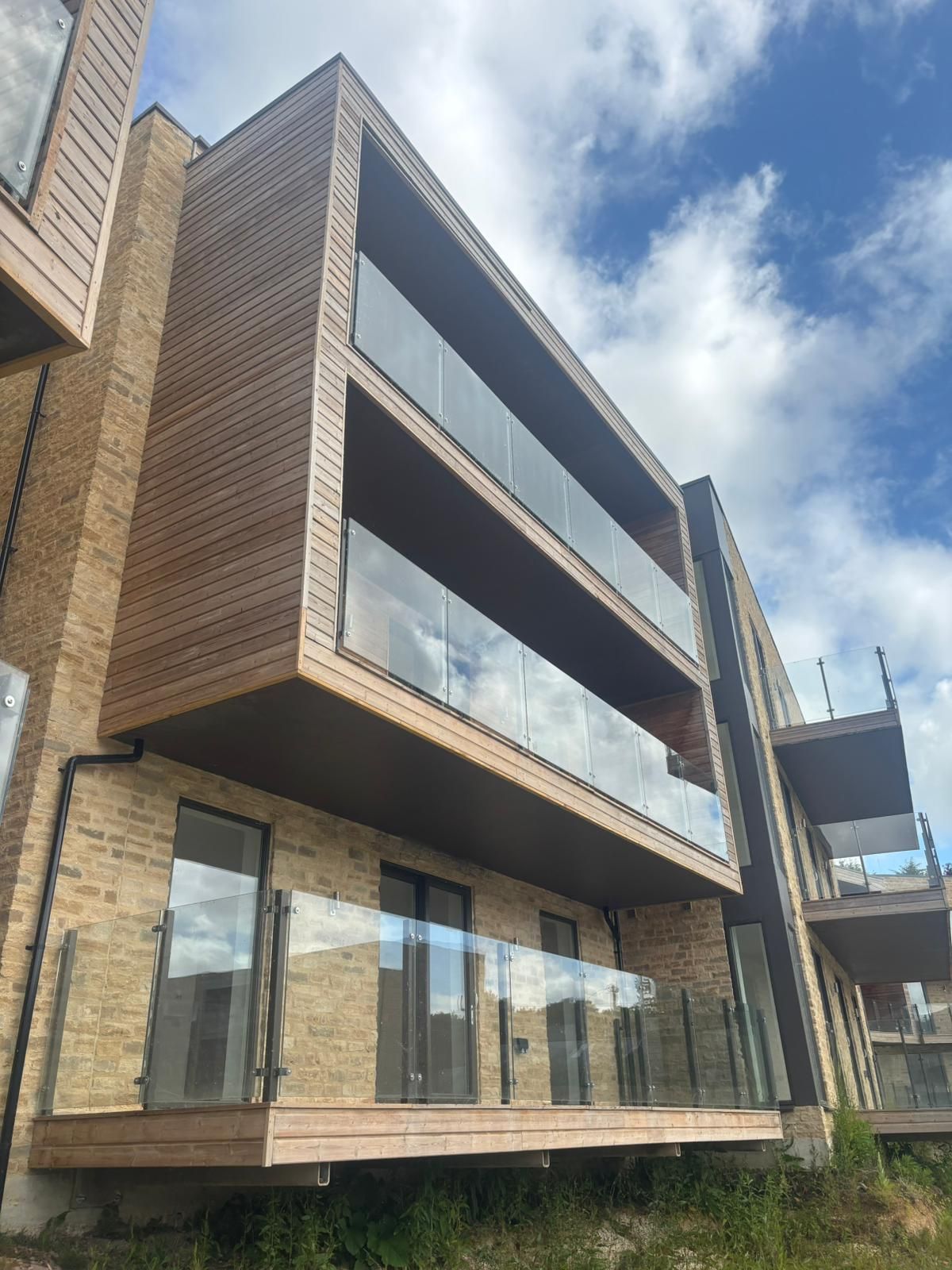 Modern building with wood and glass balconies, brick exterior, blue sky.