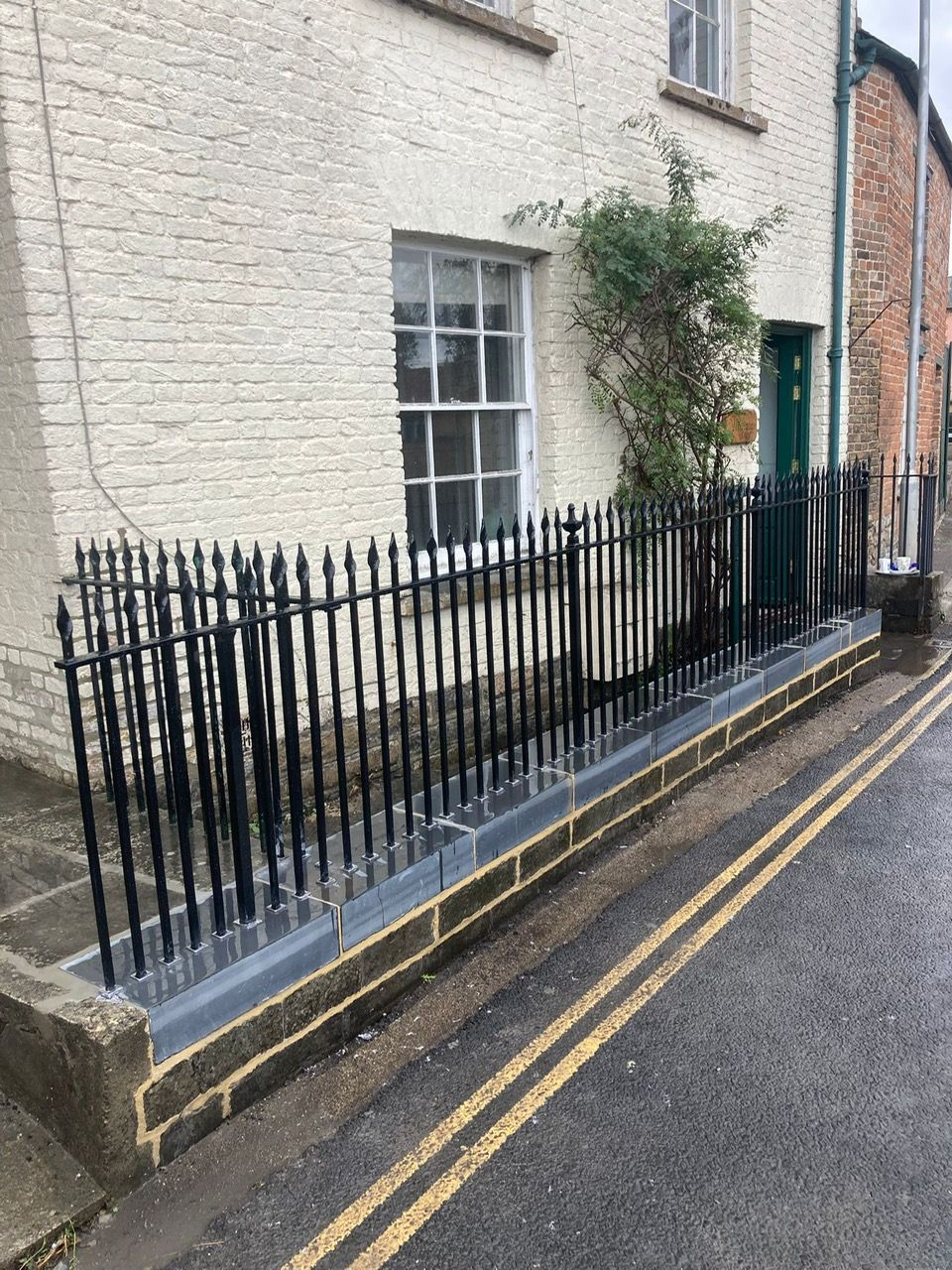 Black iron fence atop a stone wall along a street next to a white brick building.