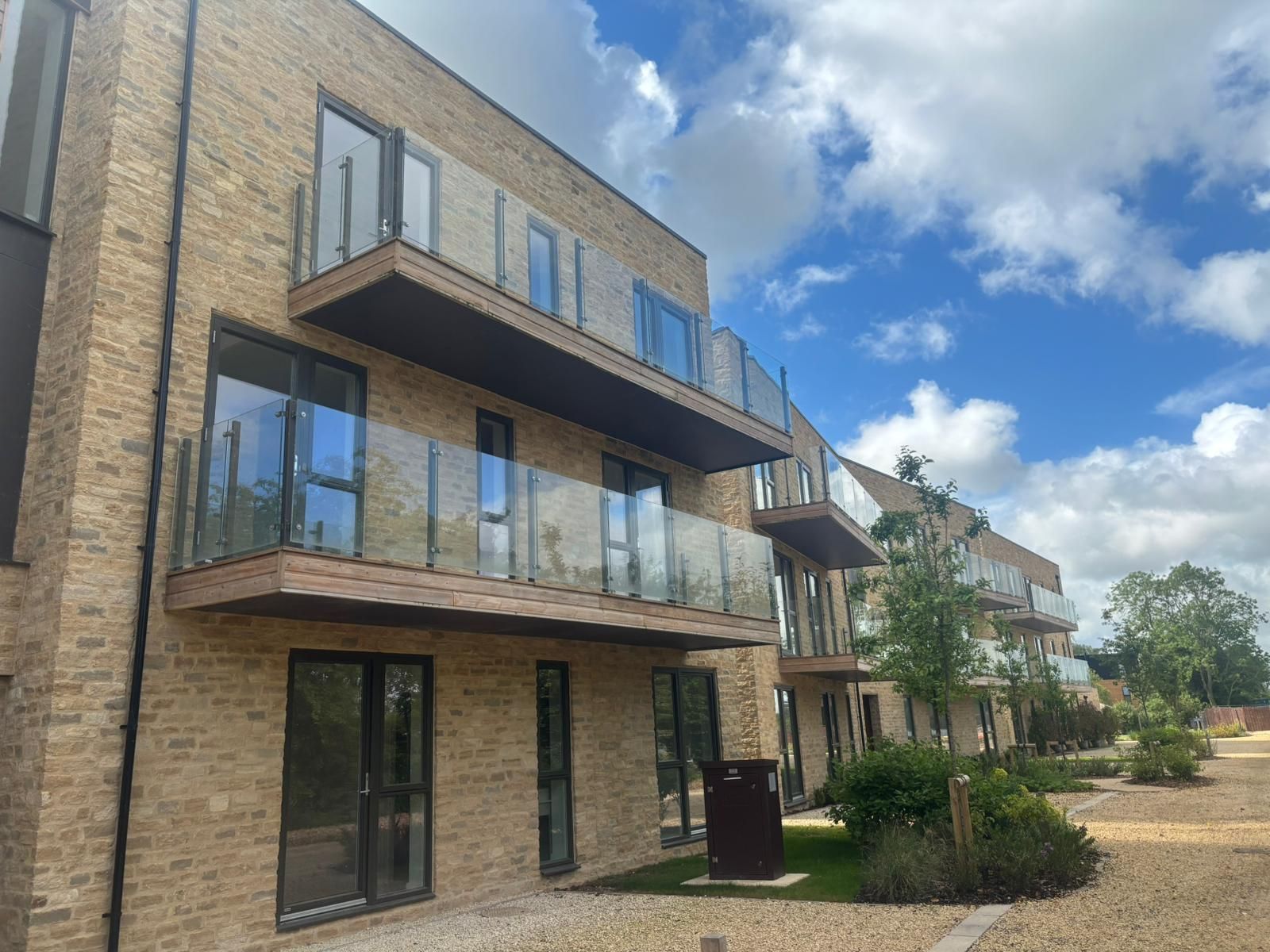 Apartment building with balconies and glass railings under a blue sky with clouds.