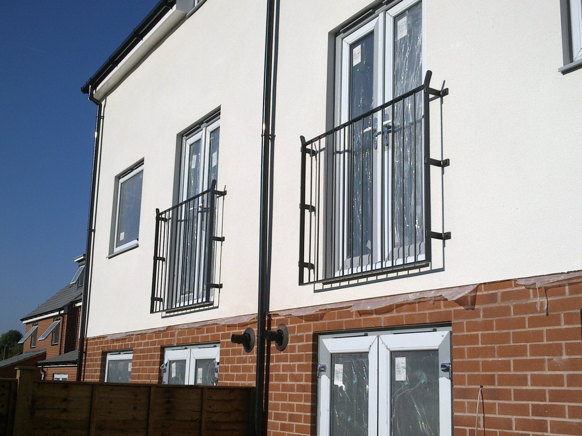 Two-story building with white stucco upper and brick lower sections. Balconies with black railings and white-framed windows.
