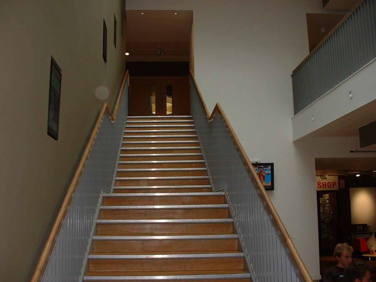 Wooden staircase in a building with metal railings and cream walls.  A doorway is at the top of the stairs.