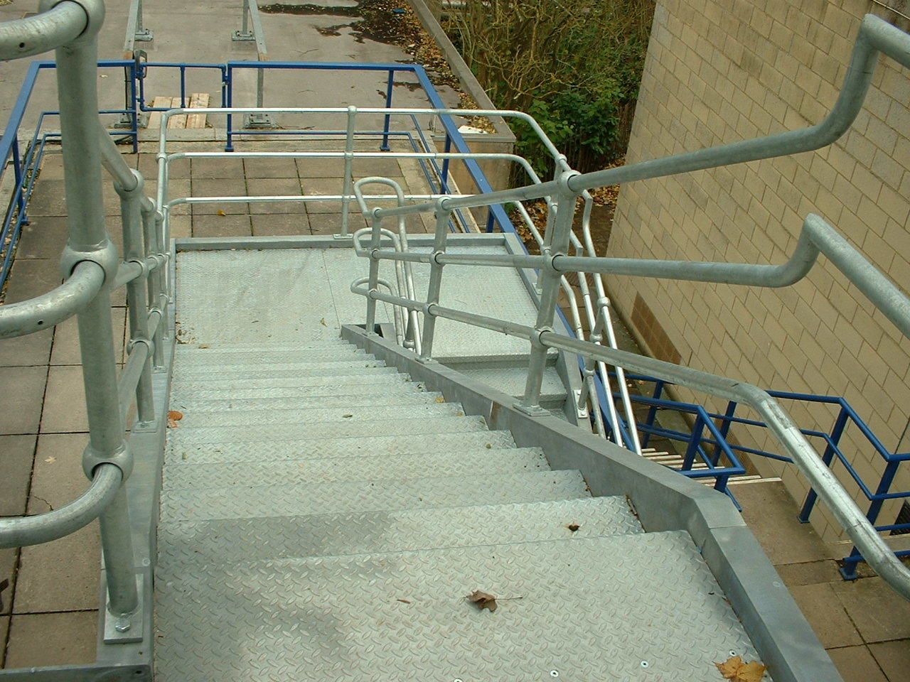 Metal staircase with railings leading down. Grey metal steps and handrails, blue railings in the background.