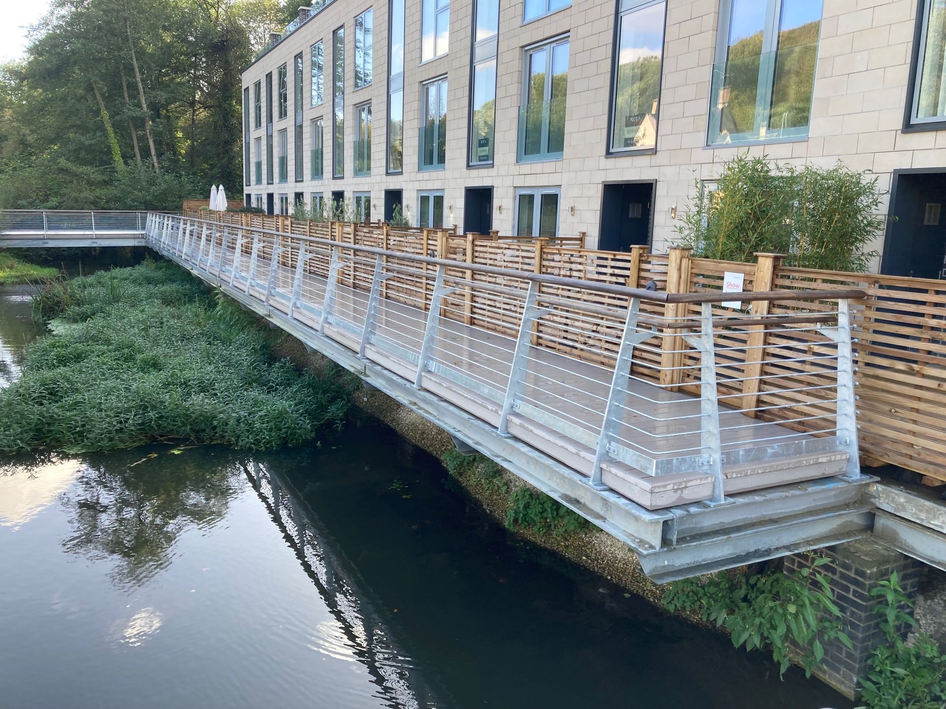 Bridge over water with wood and metal railings, connecting to a multi-story building.