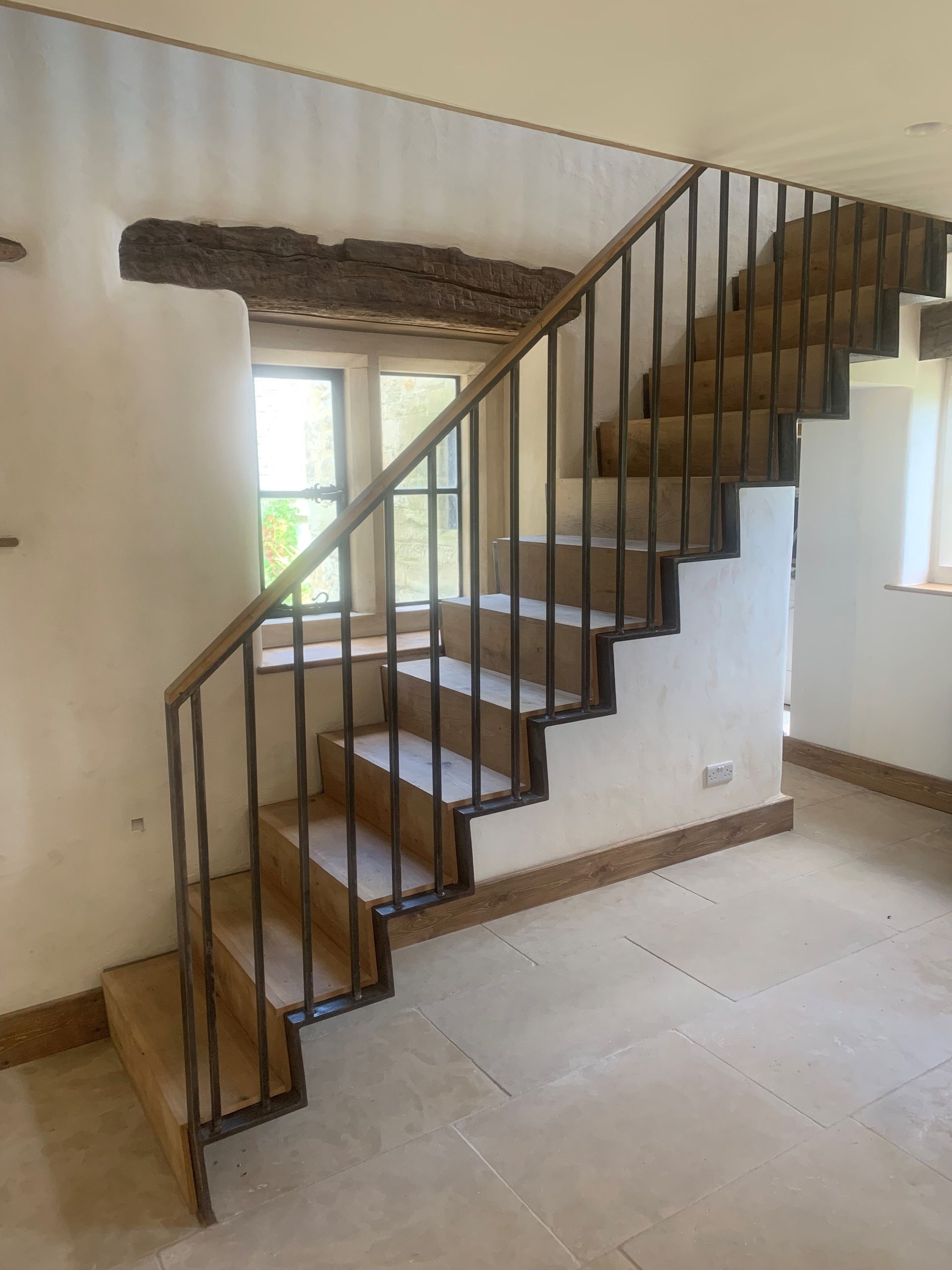Wooden staircase with dark metal railing against a white wall.