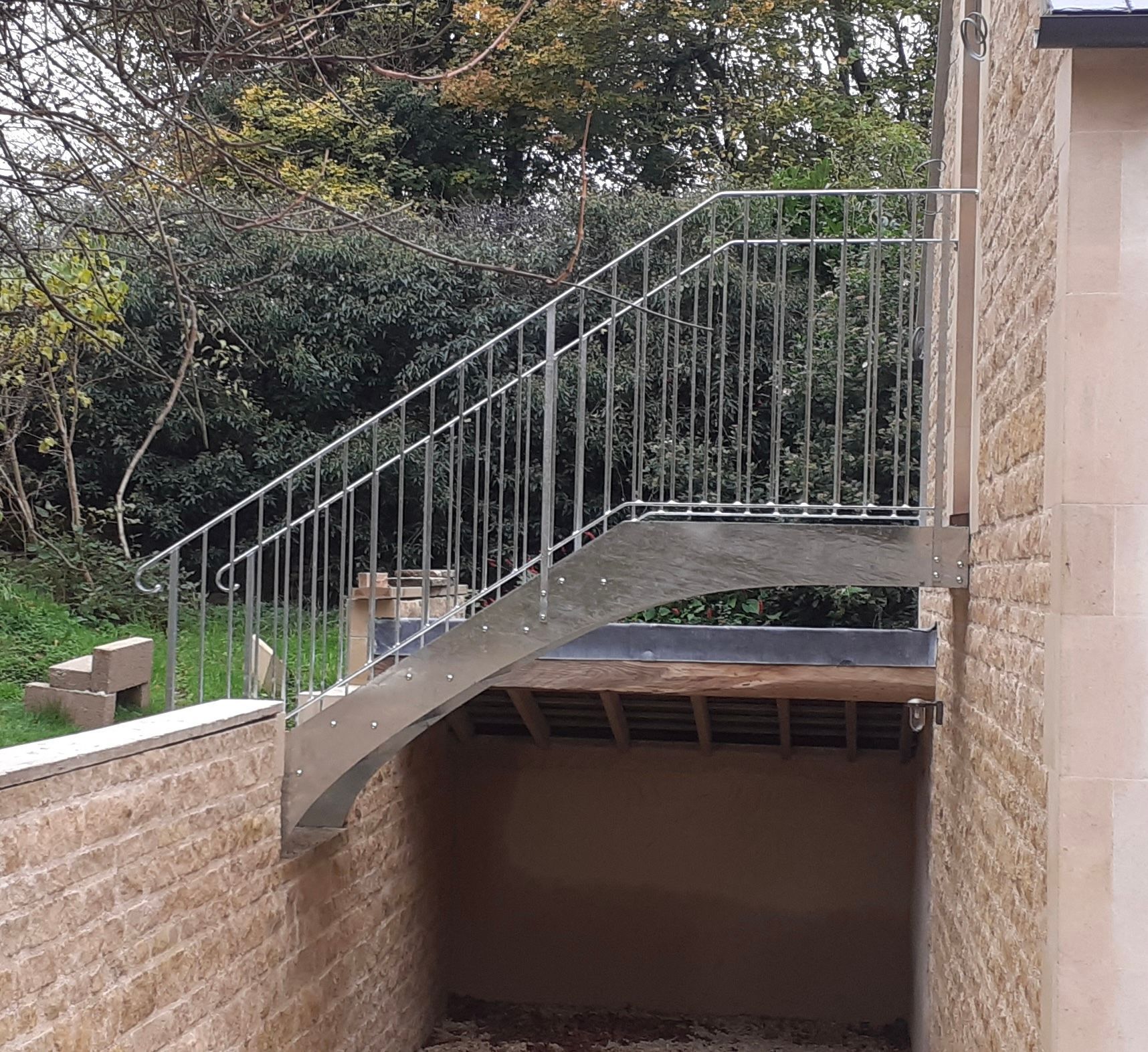 Outdoor metal staircase with railing, leading up to an elevated structure; built into a stone wall.