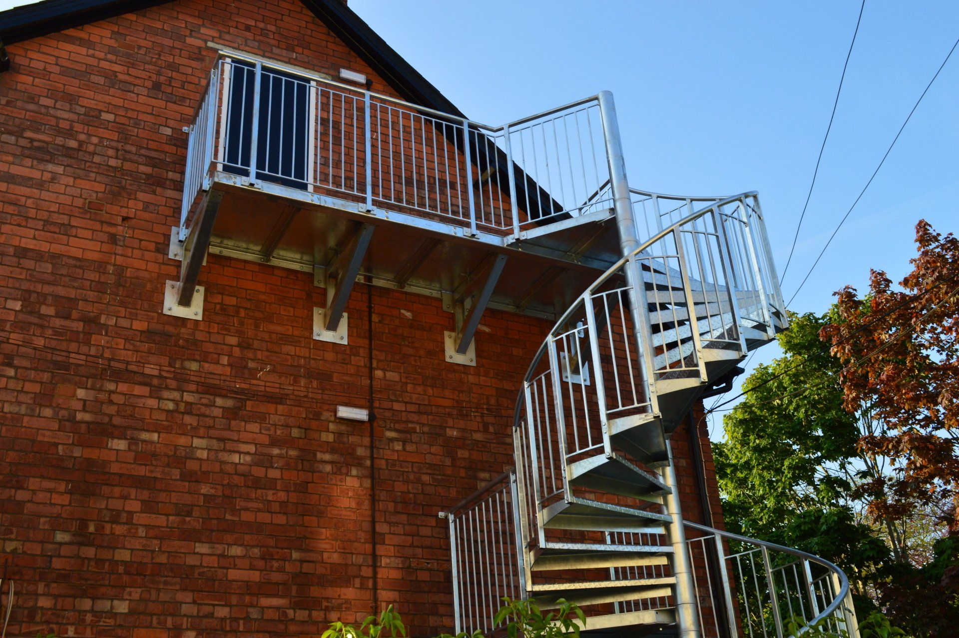 Spiral metal staircase attached to a brick building, leading to a balcony.