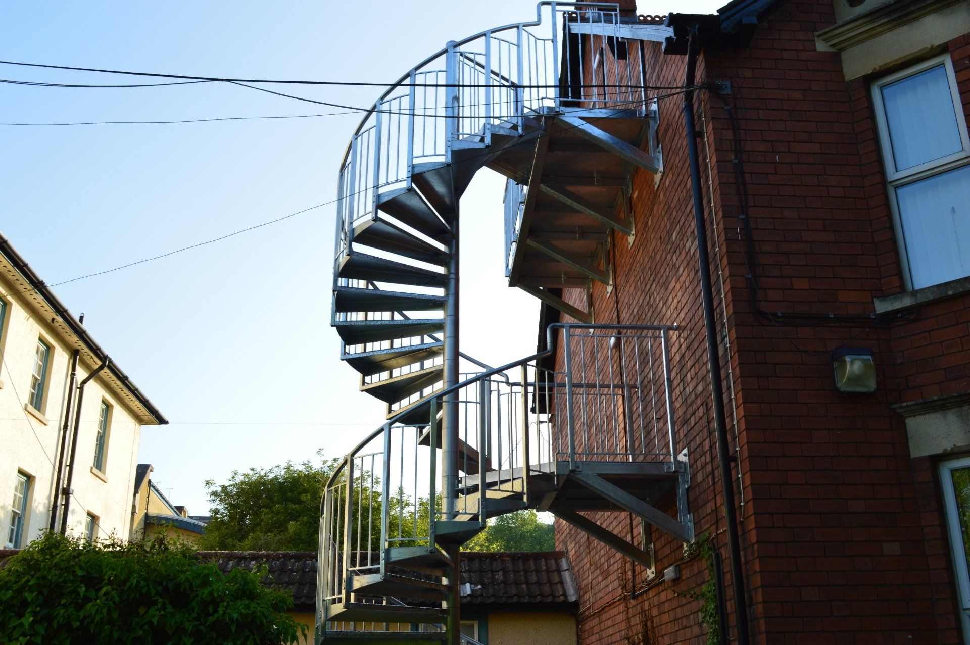 Spiral metal staircase attached to a red brick building; outdoor setting.
