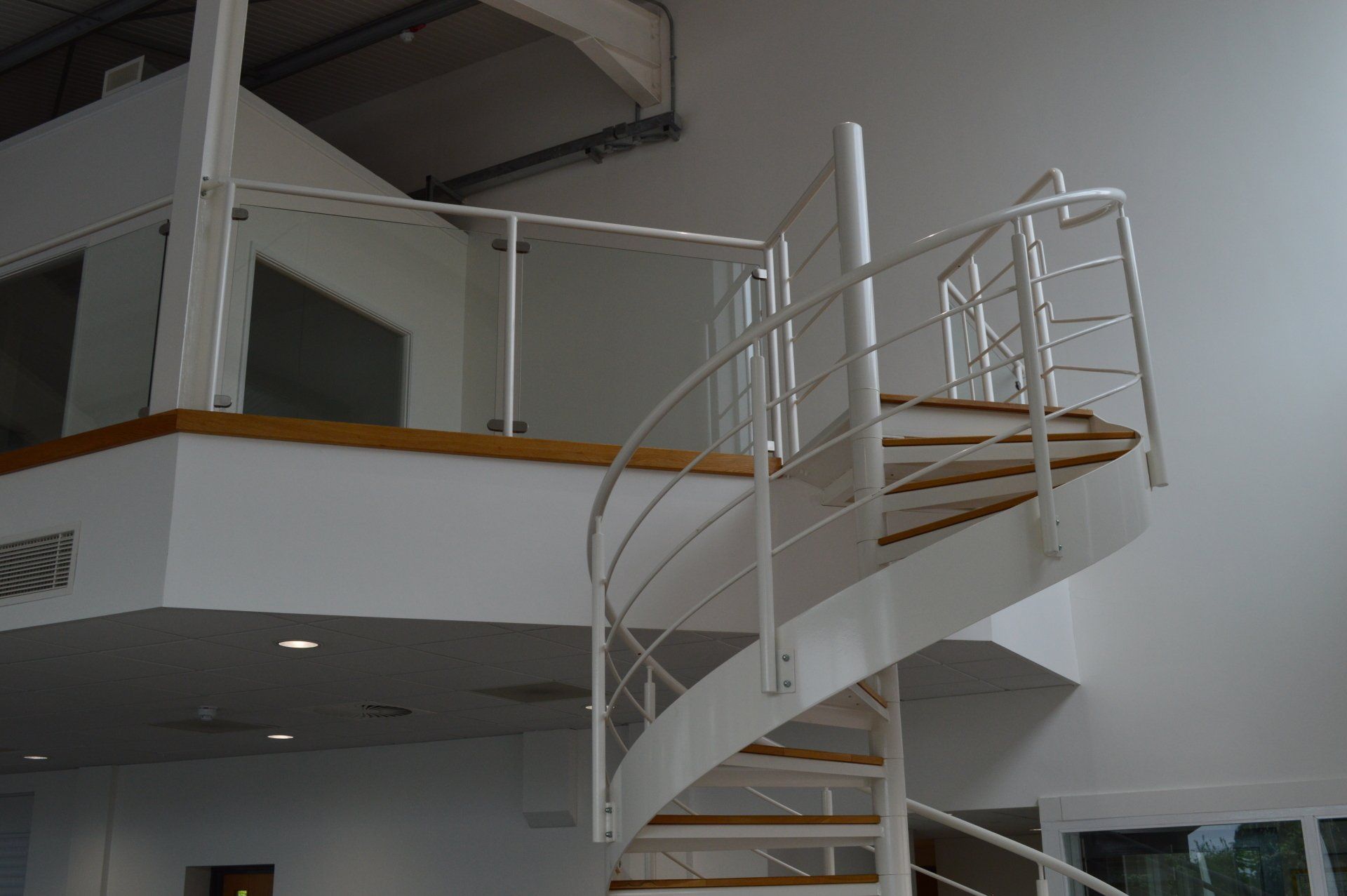 White spiral staircase with wooden steps, railing, and a second-story landing.