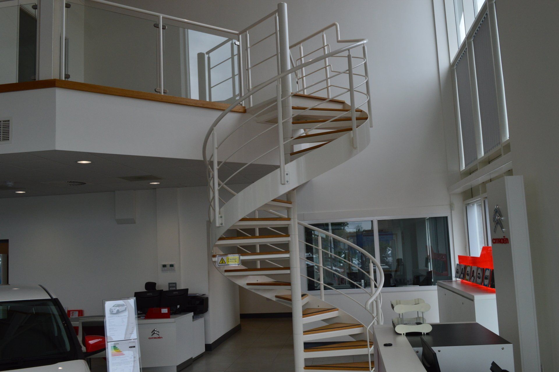 Spiral staircase with wooden steps, white railing, and a mezzanine in a modern building.