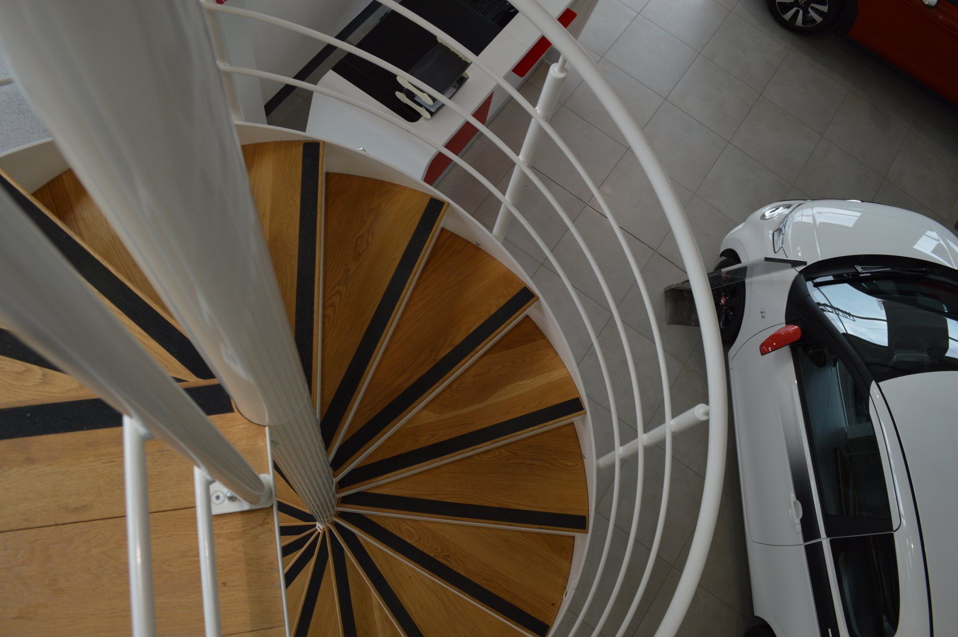Spiral staircase with white railing, wooden steps, and a white car.