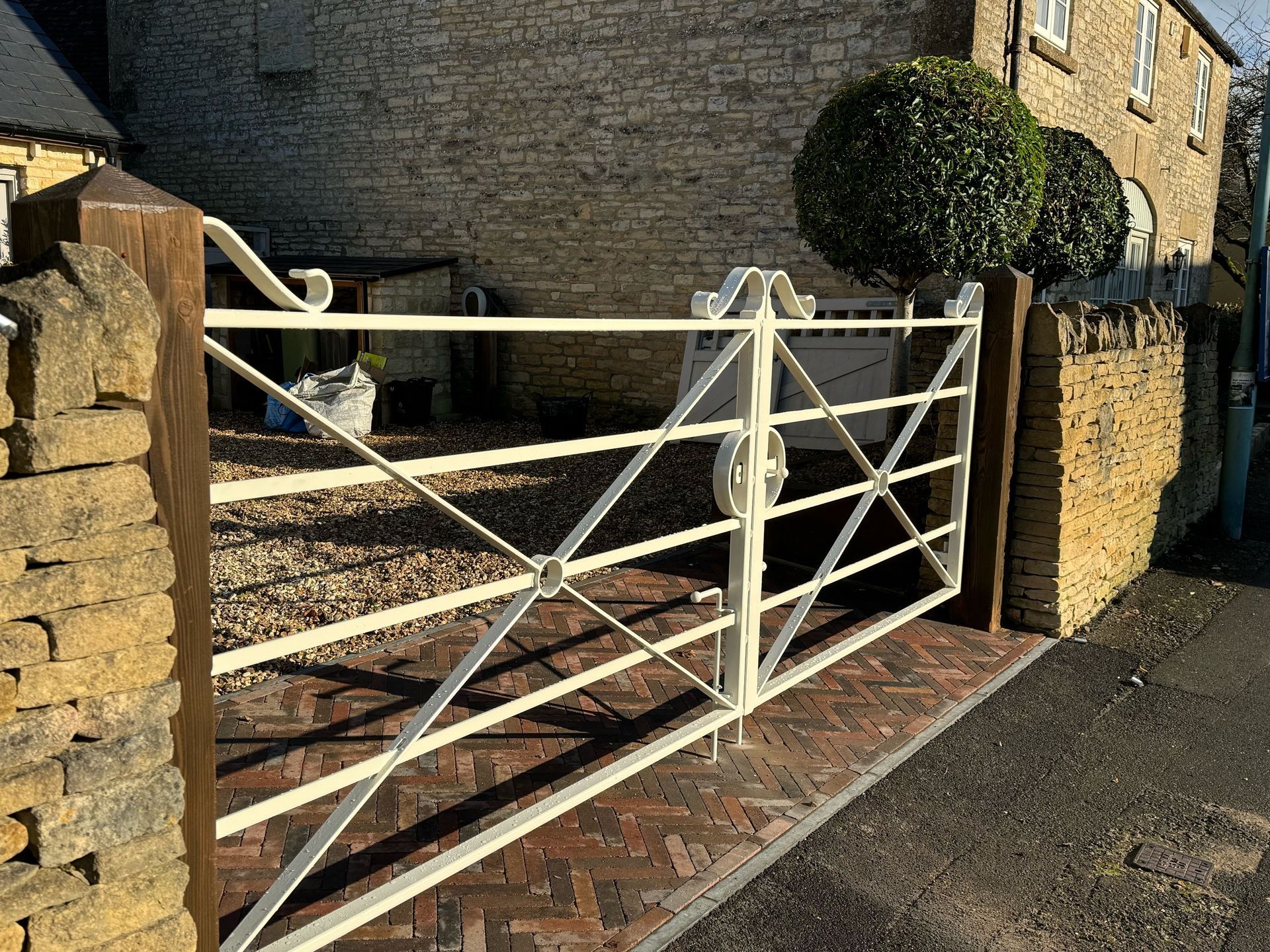 Cream-colored metal gate with decorative scrollwork between stone pillars. Brick walkway in front.