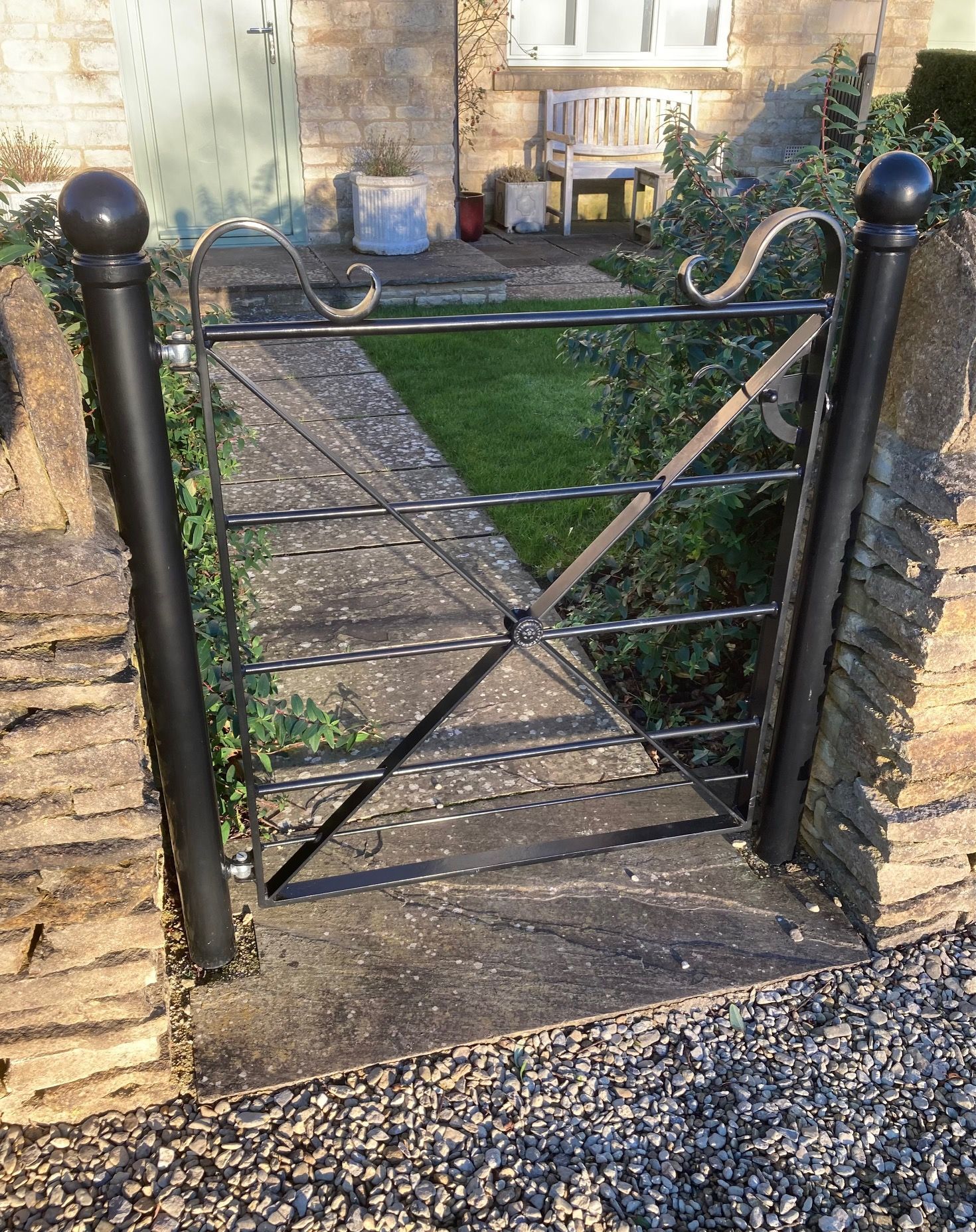 Black wrought iron gate set in a stone wall, leading to a garden.