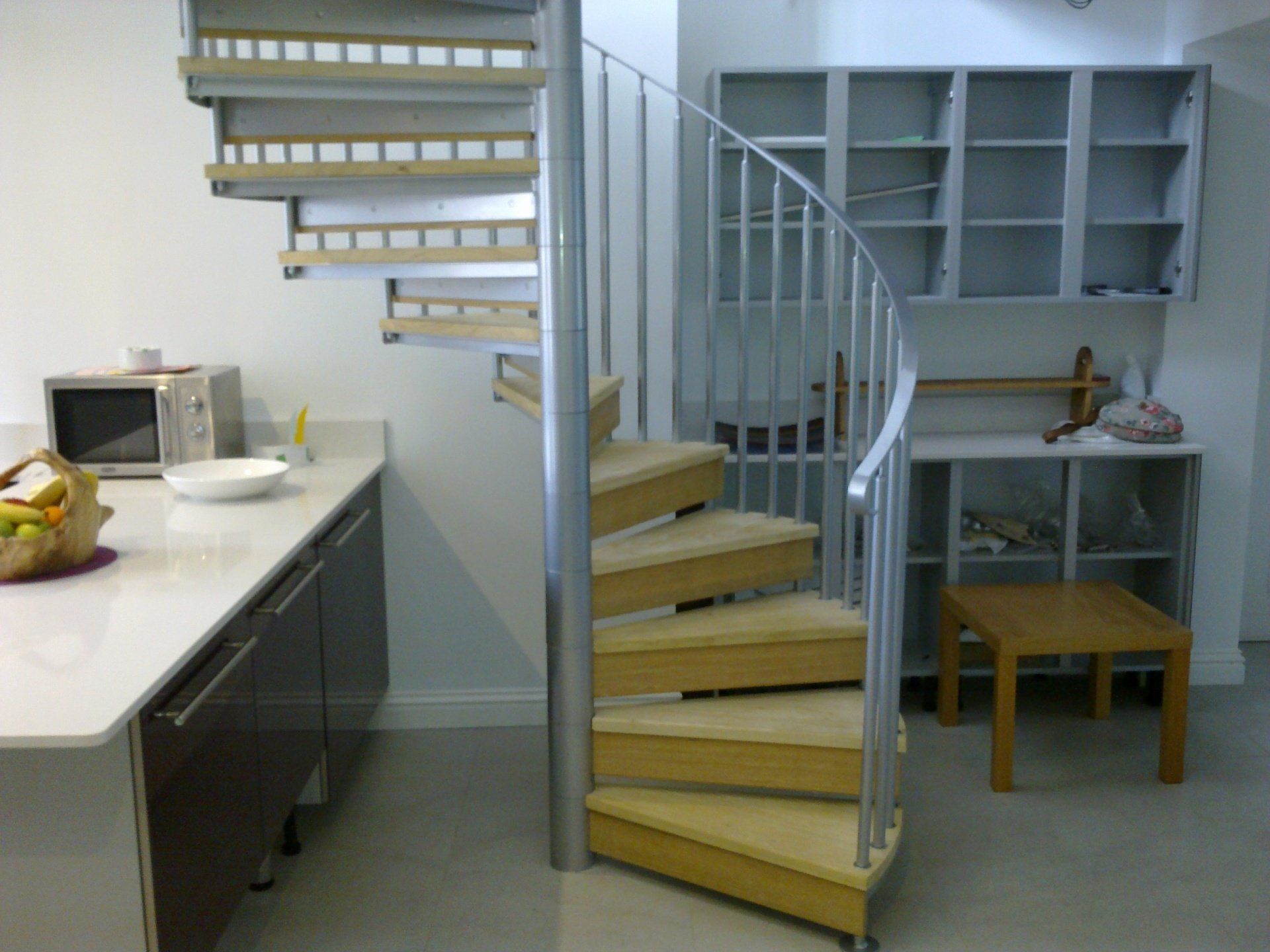 Spiral staircase with wooden steps and metal railing in a kitchen setting.