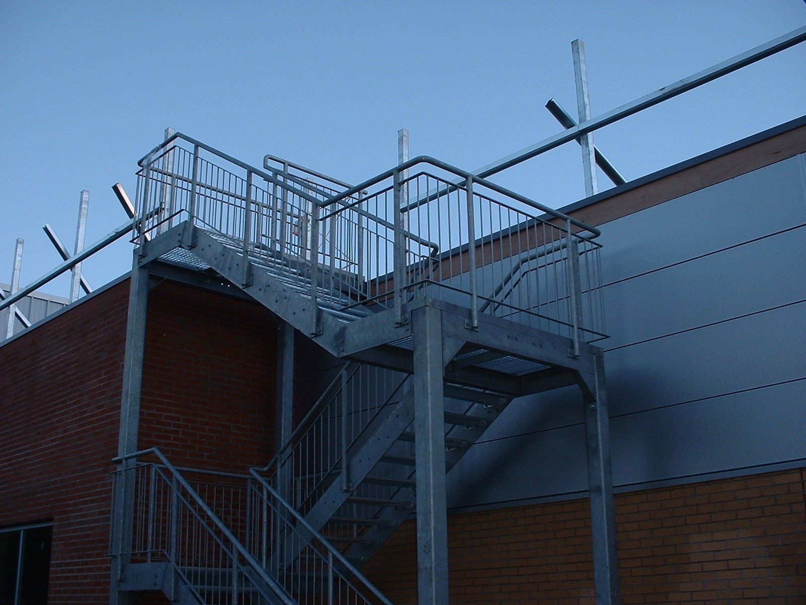 Metal fire escape stairs on a brick and white-paneled building exterior against a clear blue sky.