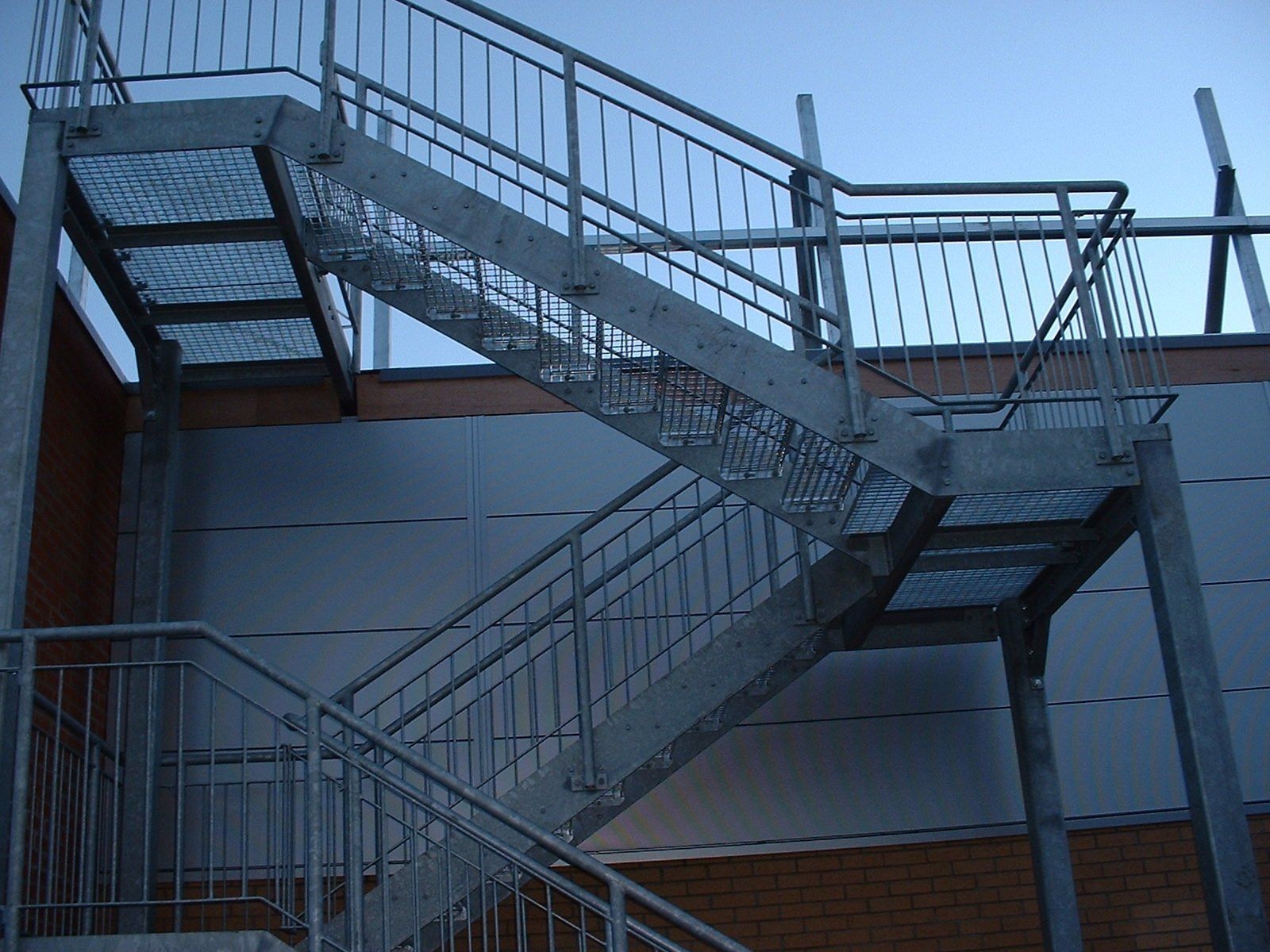 Exterior metal staircase against a building with brick and white panels.