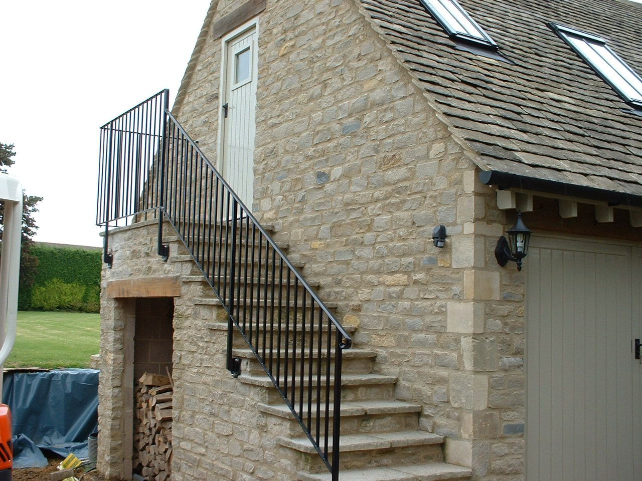 Stone building with exterior stairs and black metal railing leading to a door.