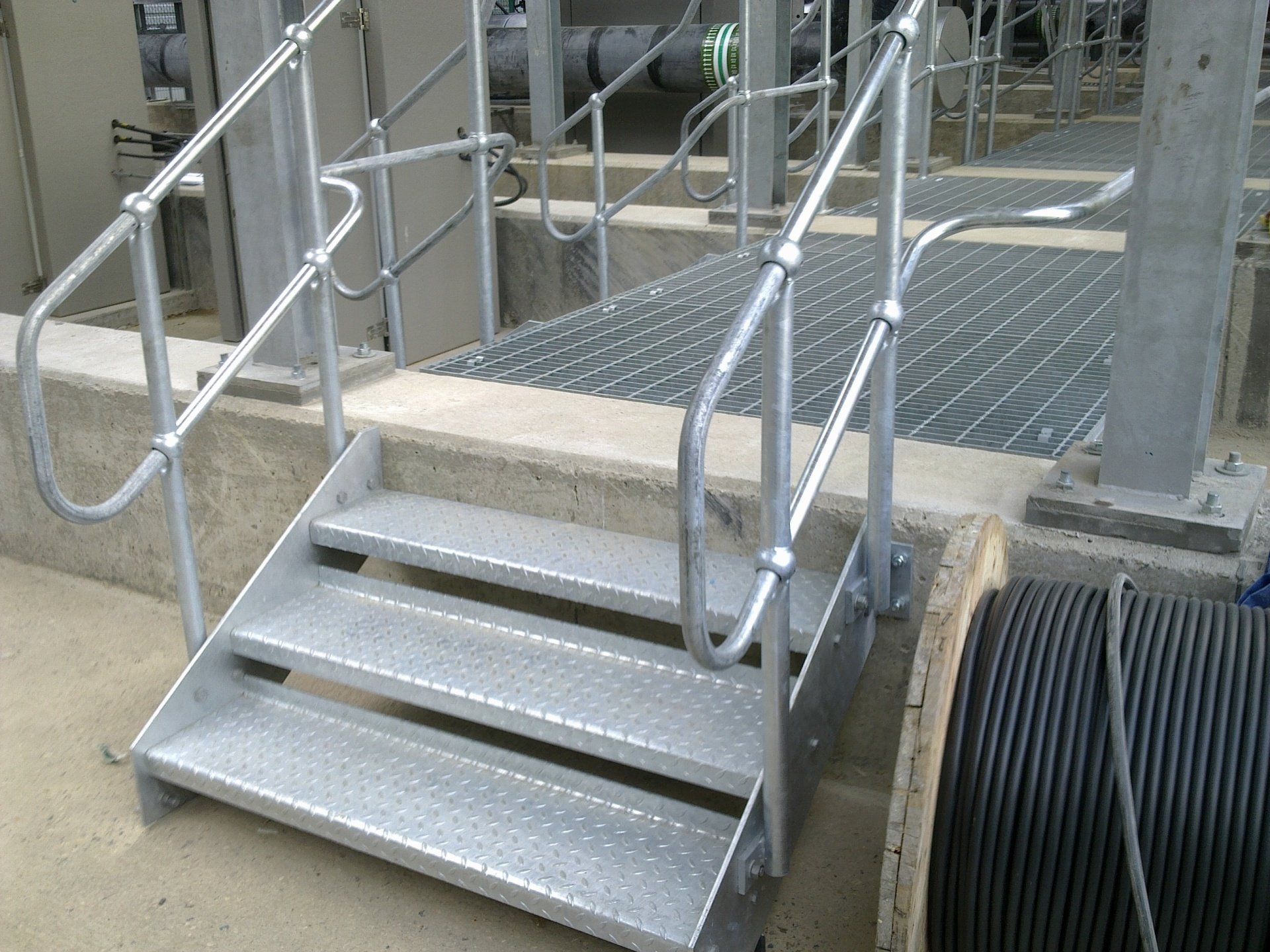 Metal staircase with handrails leading to a grated walkway.