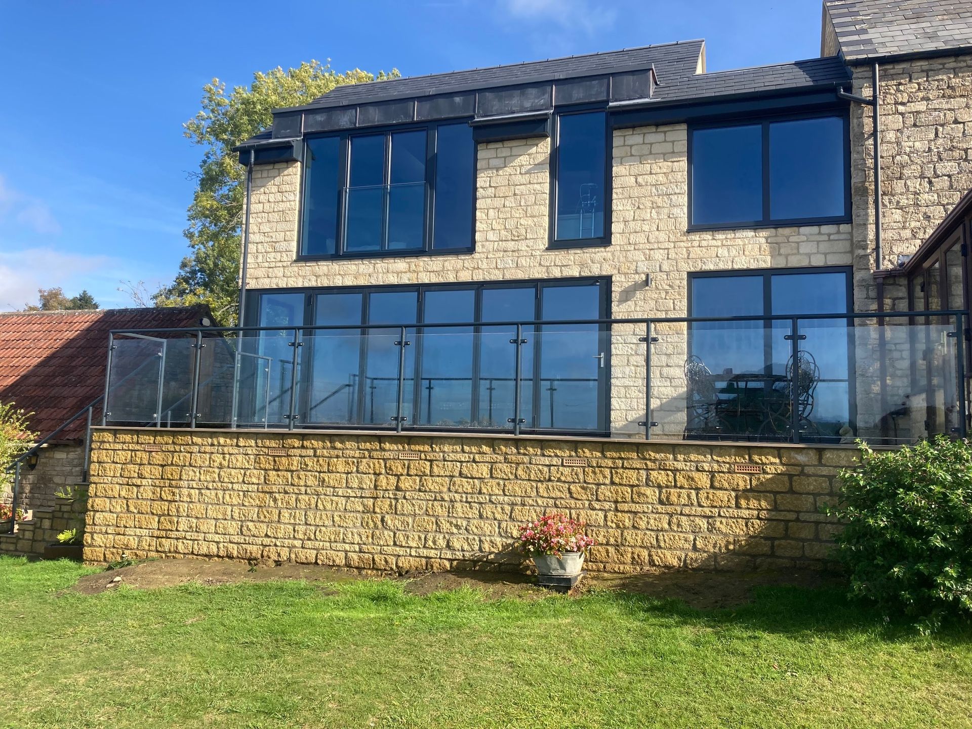 Two-story stone building with large, dark-framed windows and a glass balcony, set against a blue sky.