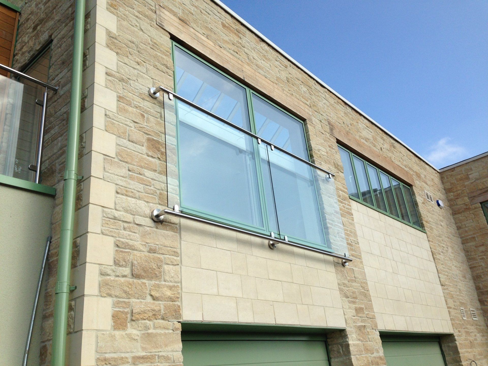 Building exterior with glass balcony and stone facade against a blue sky.
