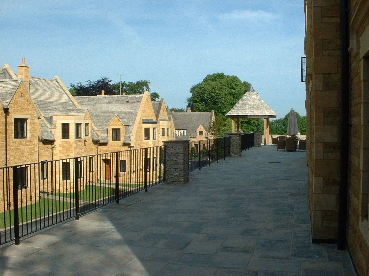 Stone patio with wrought iron railing overlooking townhouses with brown stone and gray rooftops.