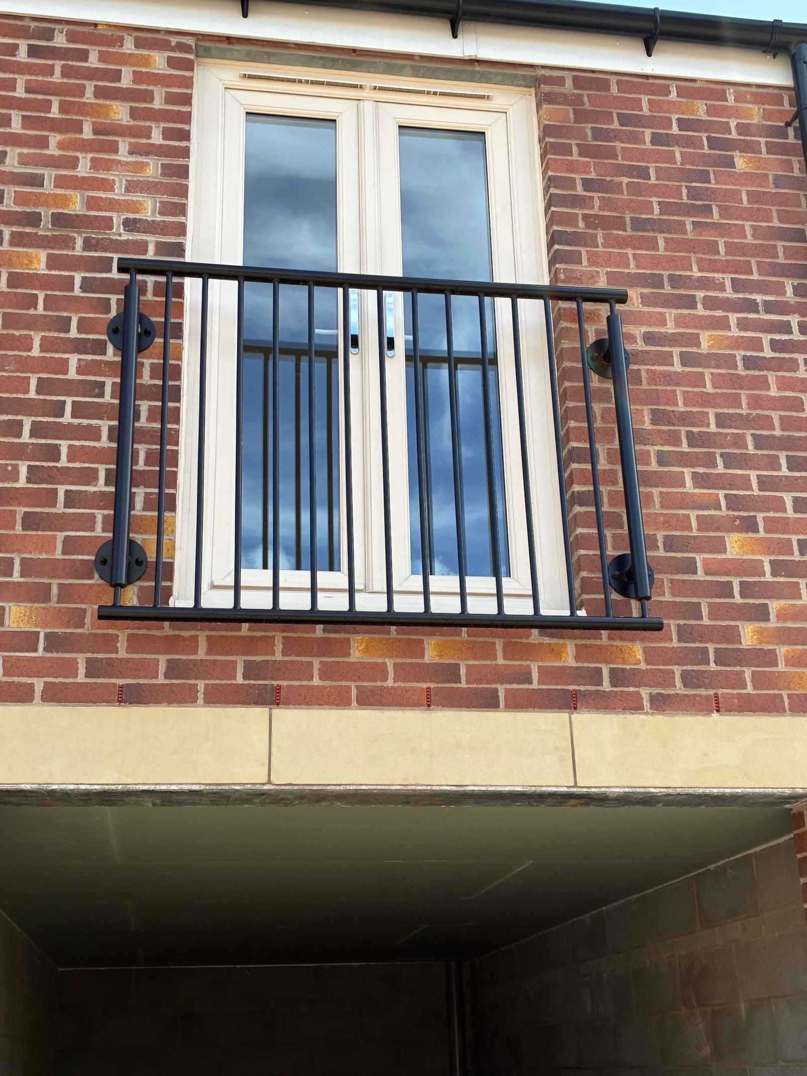 Black iron balcony railing on brick building exterior. Double glass doors above open space.