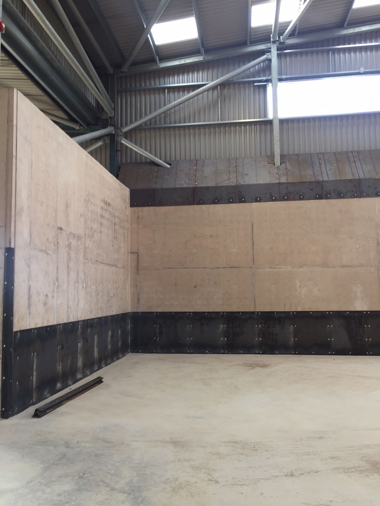 Interior of a large building with plywood walls and a concrete floor. Steel beams and a skylight are visible.