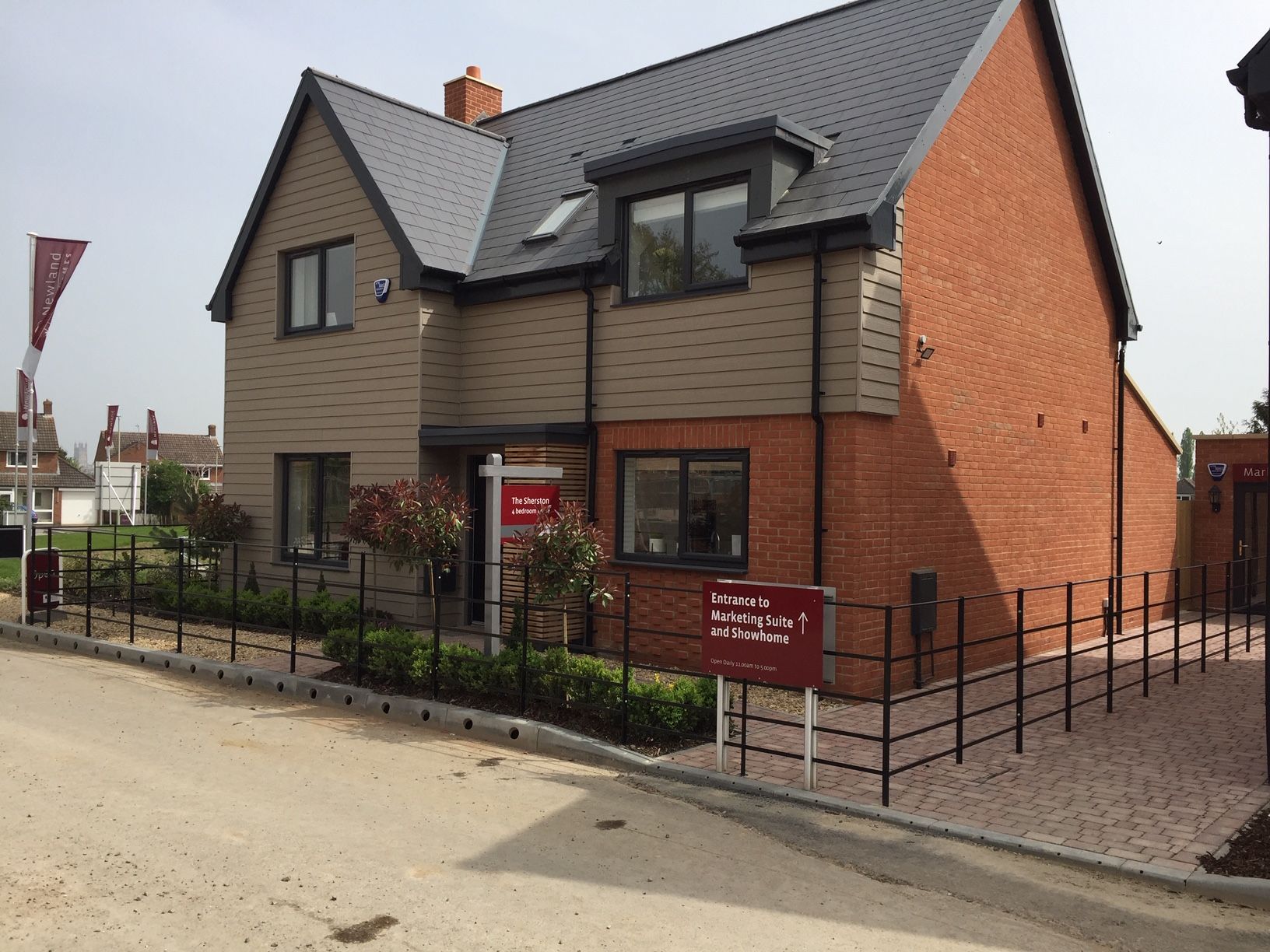 New house exterior with brick and tan siding, black roof, and small front yard with metal fencing.
