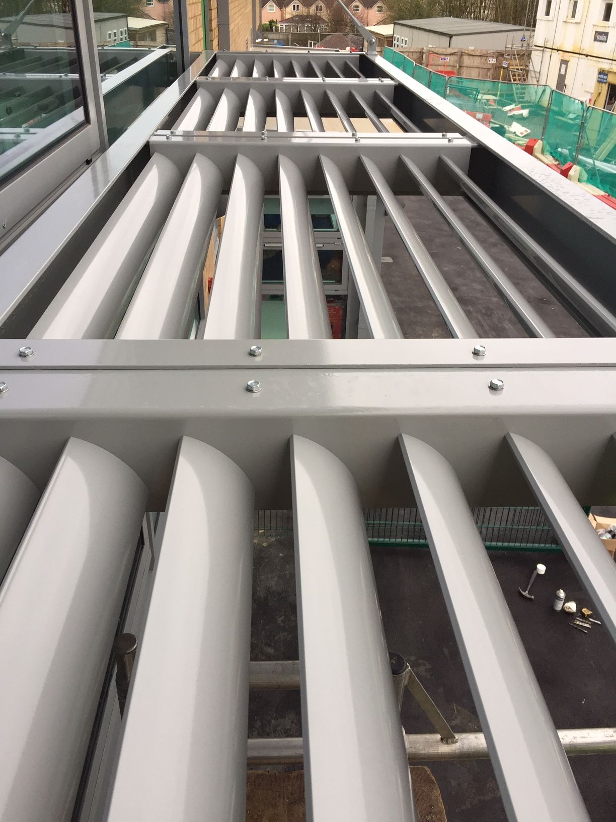 Overhead view of a modern building's ventilation louvers. Silver metal blades provide shade.