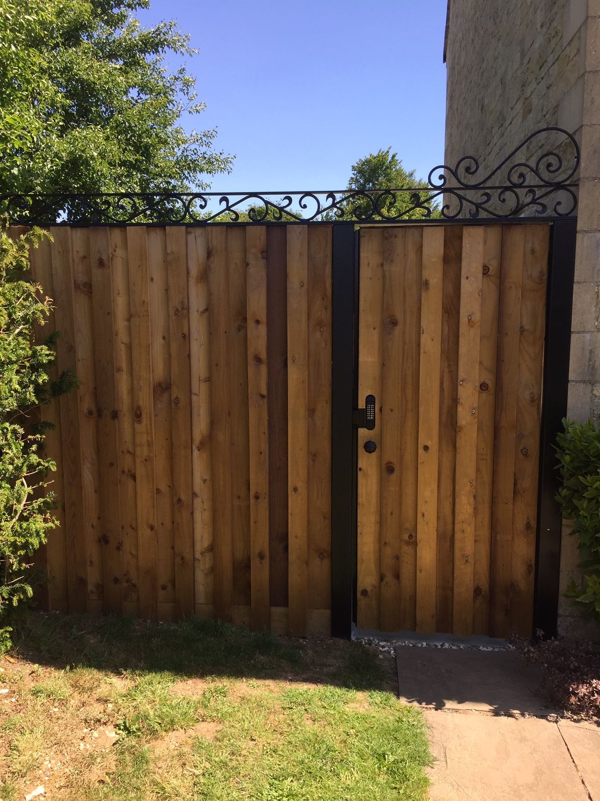 Wooden gate with black metal frame and decorative ironwork topper.