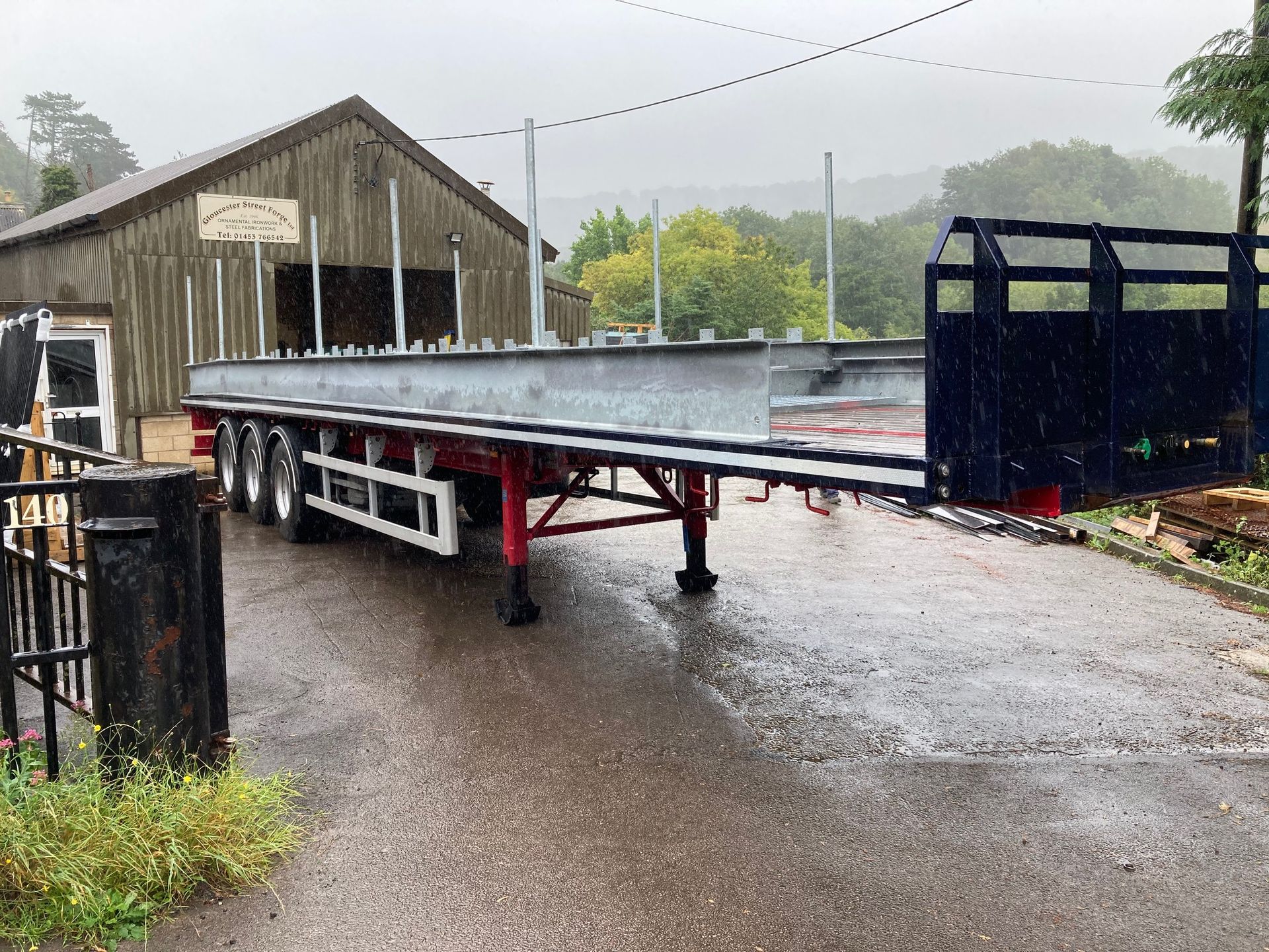 A flatbed trailer parked on a wet street next to a wooden building on a rainy day.