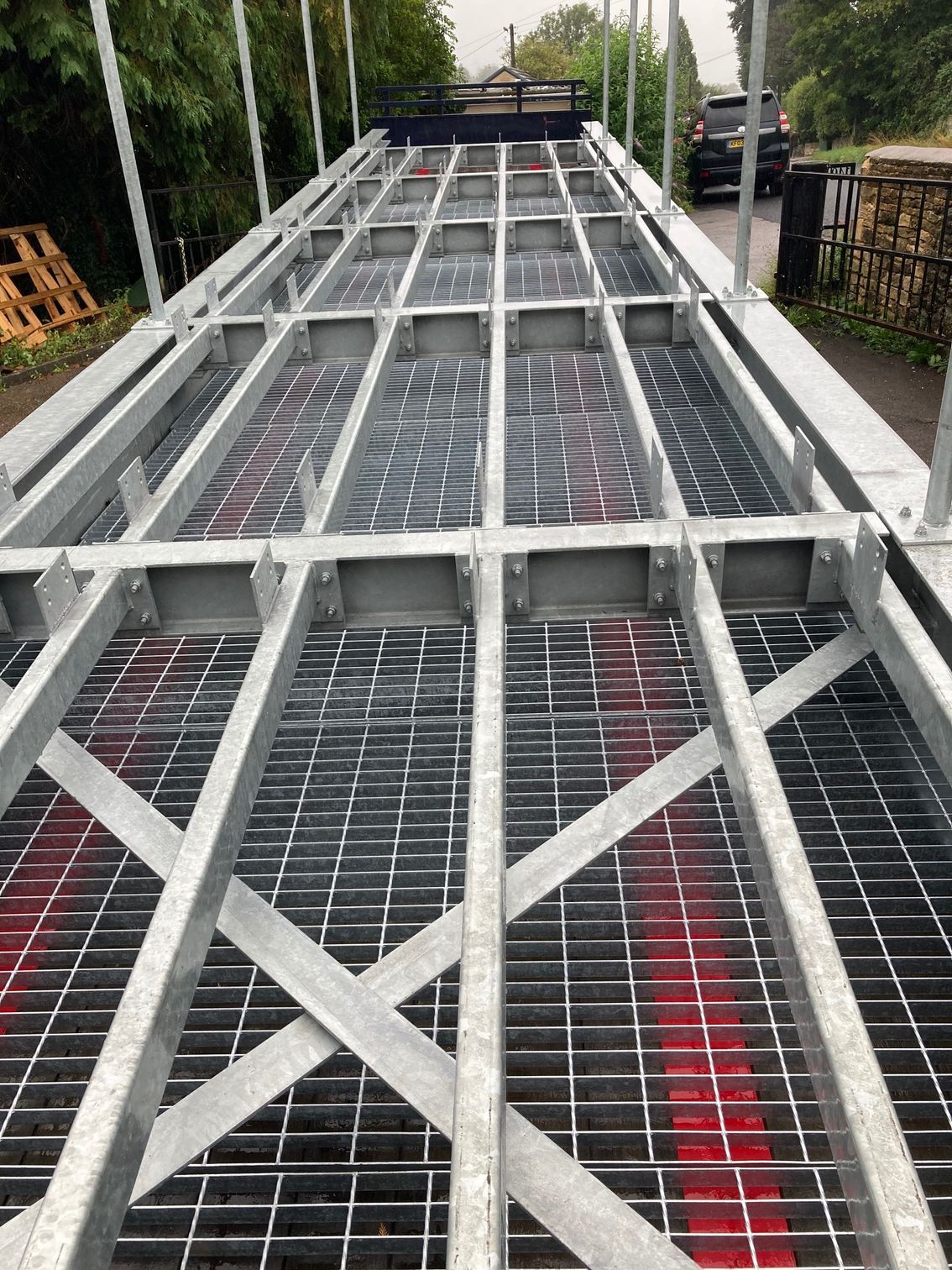 Metal grid flooring on a flatbed trailer, viewed from front. Red paint visible. Roadside setting.