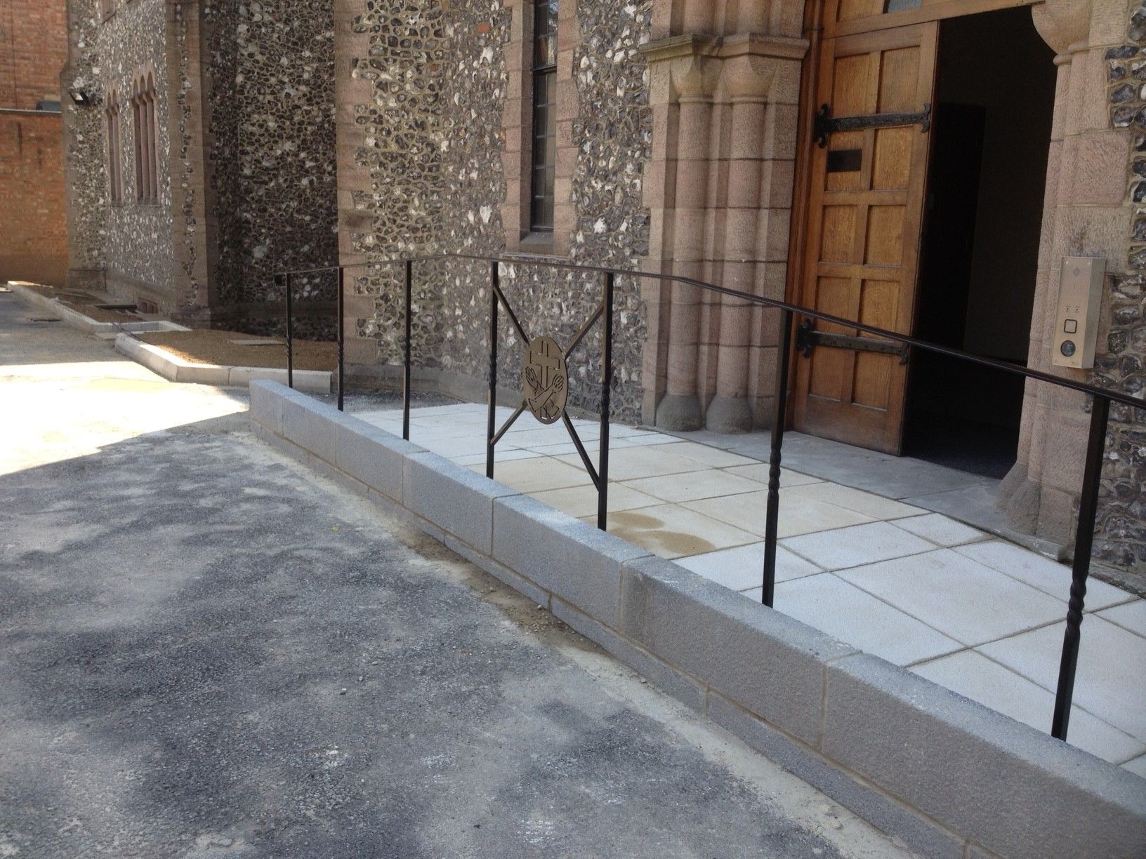 Exterior view of church entrance with ramp and black railing. Gray stone building and pavement.