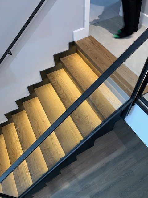 Wooden staircase with built-in lights, black railing, and a person's feet visible at the top.