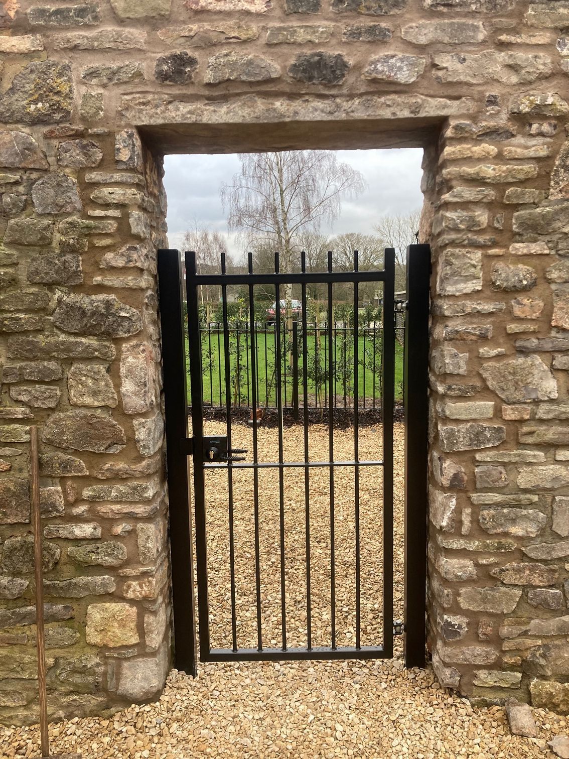 Black metal gate set in a stone wall, leading to a grassy field.