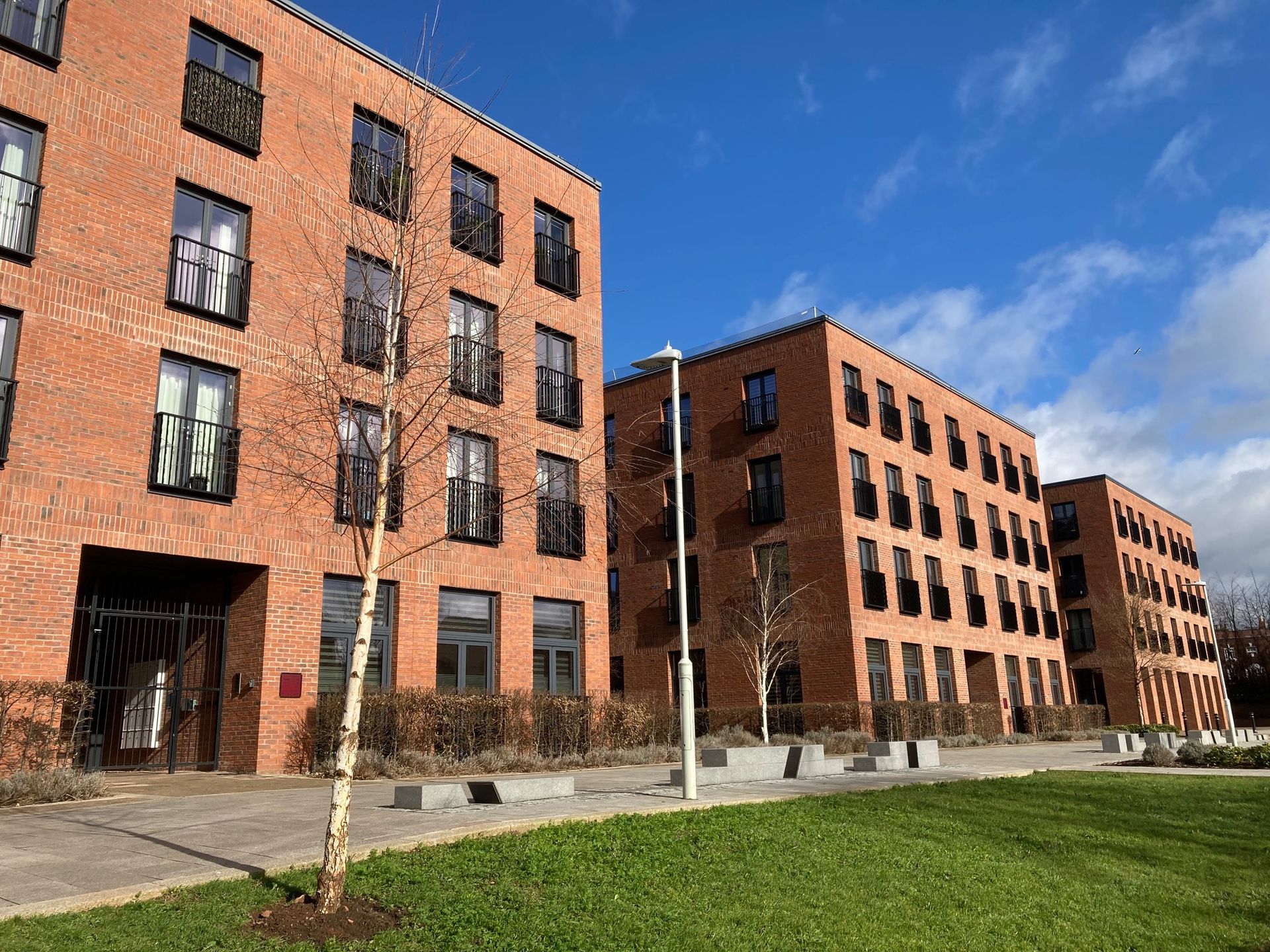 Three red brick apartment buildings against a blue sky, with a small lawn in front.