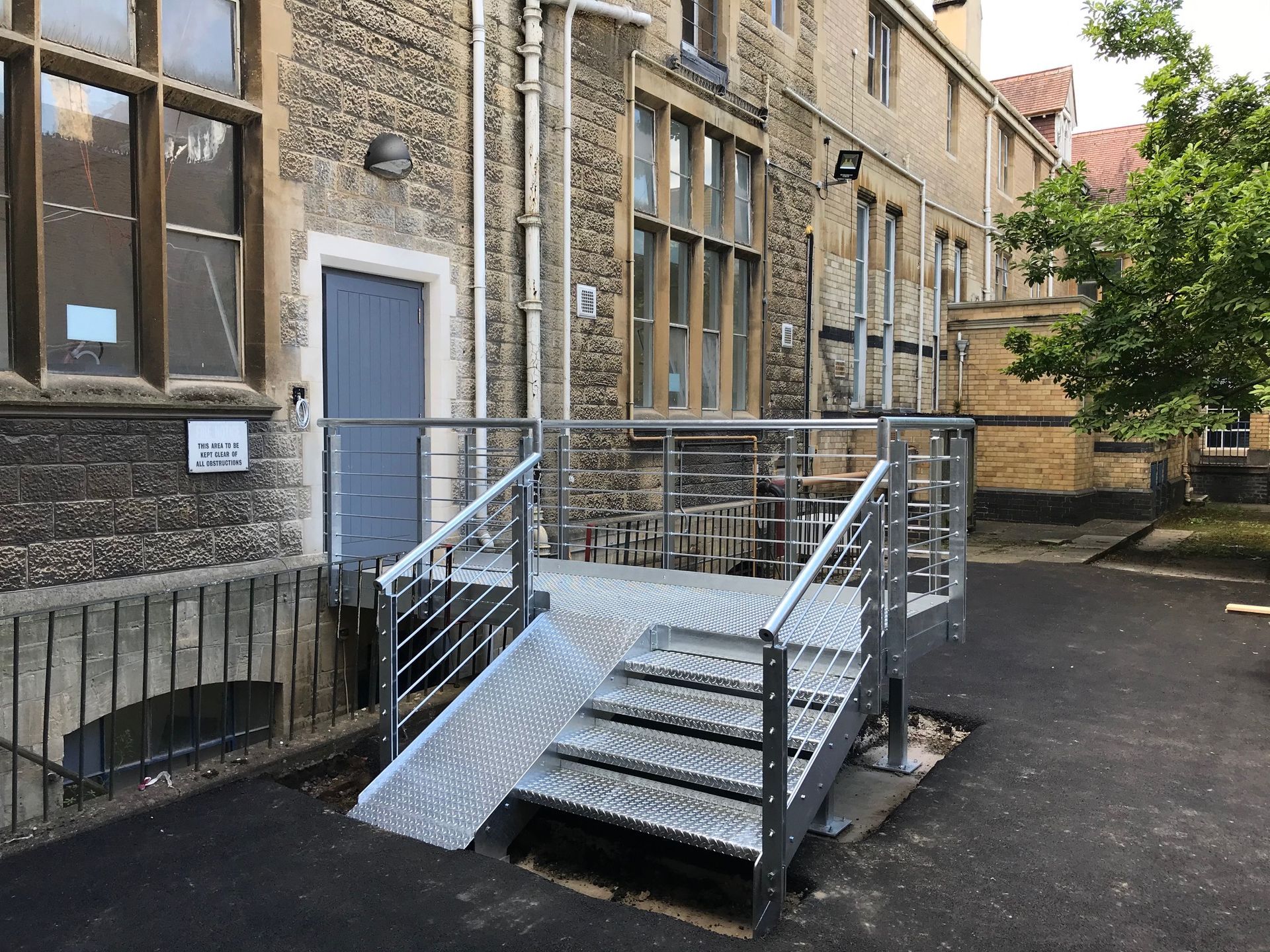 Metal ramp and steps provide accessible entry to a stone building with a blue door.