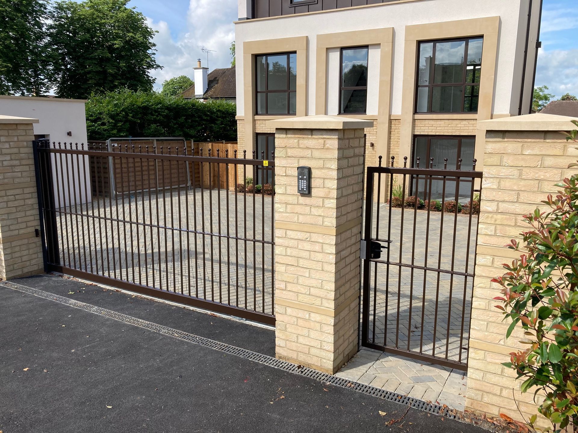 Iron gate and brick pillars in front of a modern beige building.