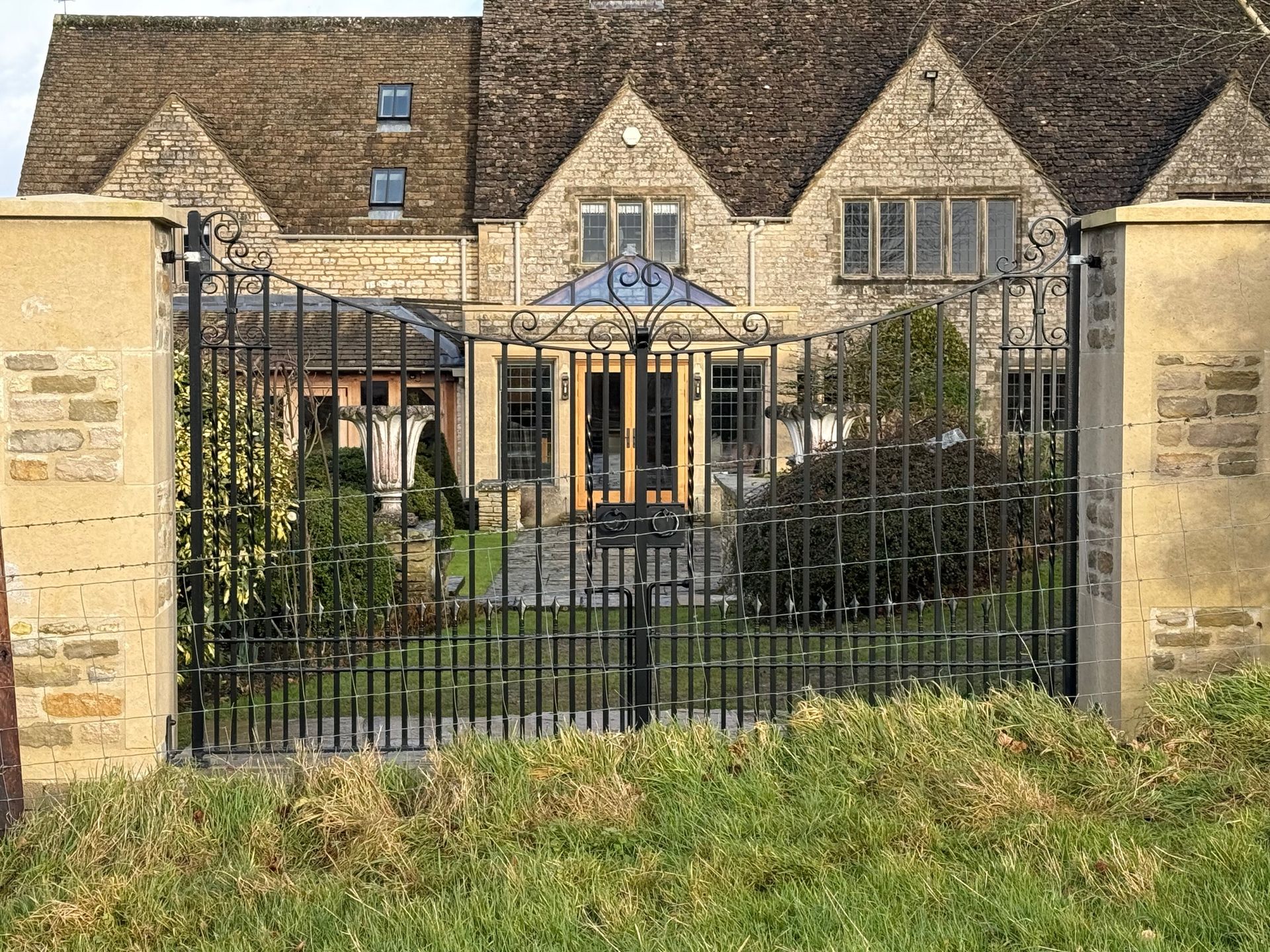 Black wrought-iron gates in front of a stone house with a tiled roof.