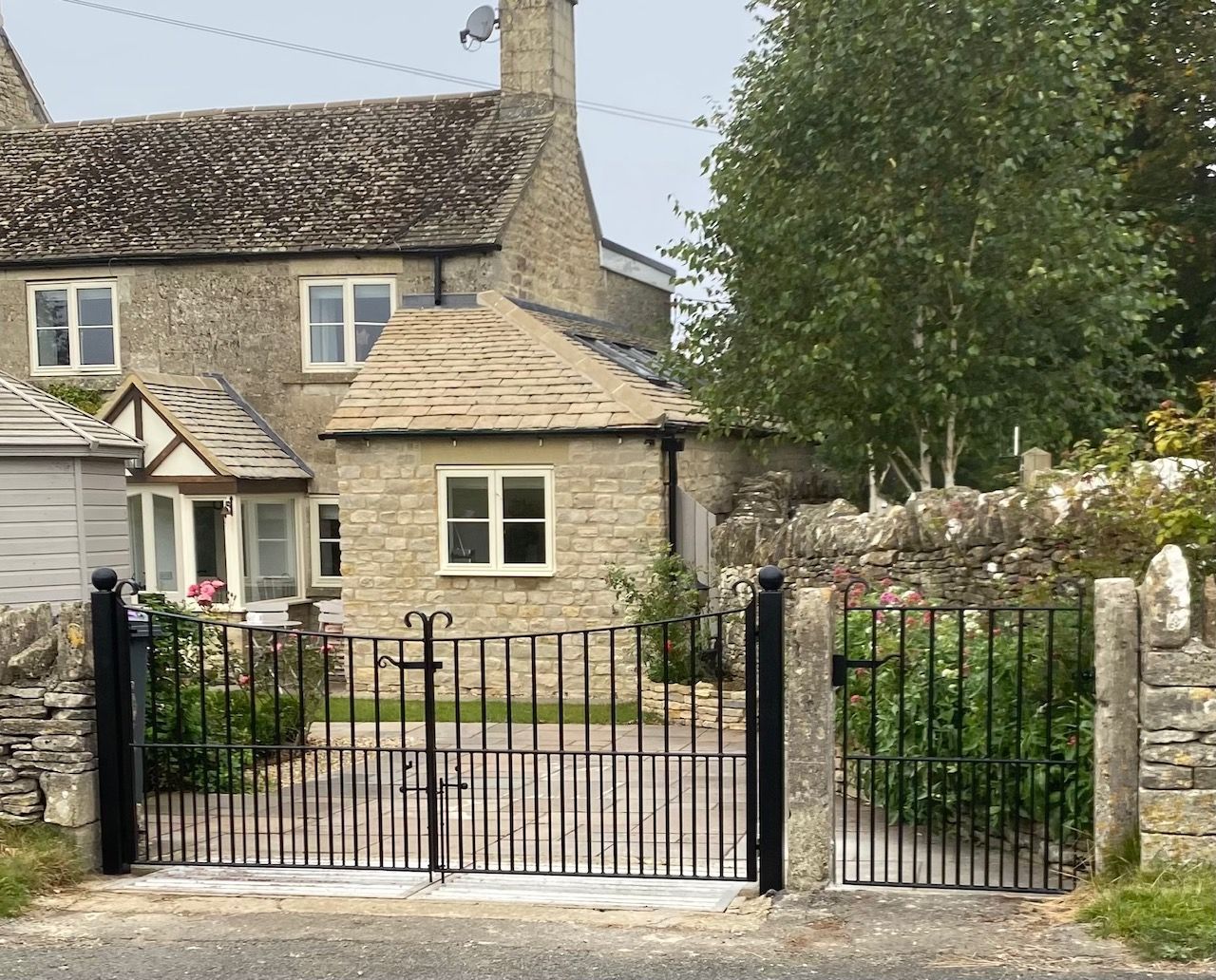 Black iron gates open onto a stone house with a slate roof.