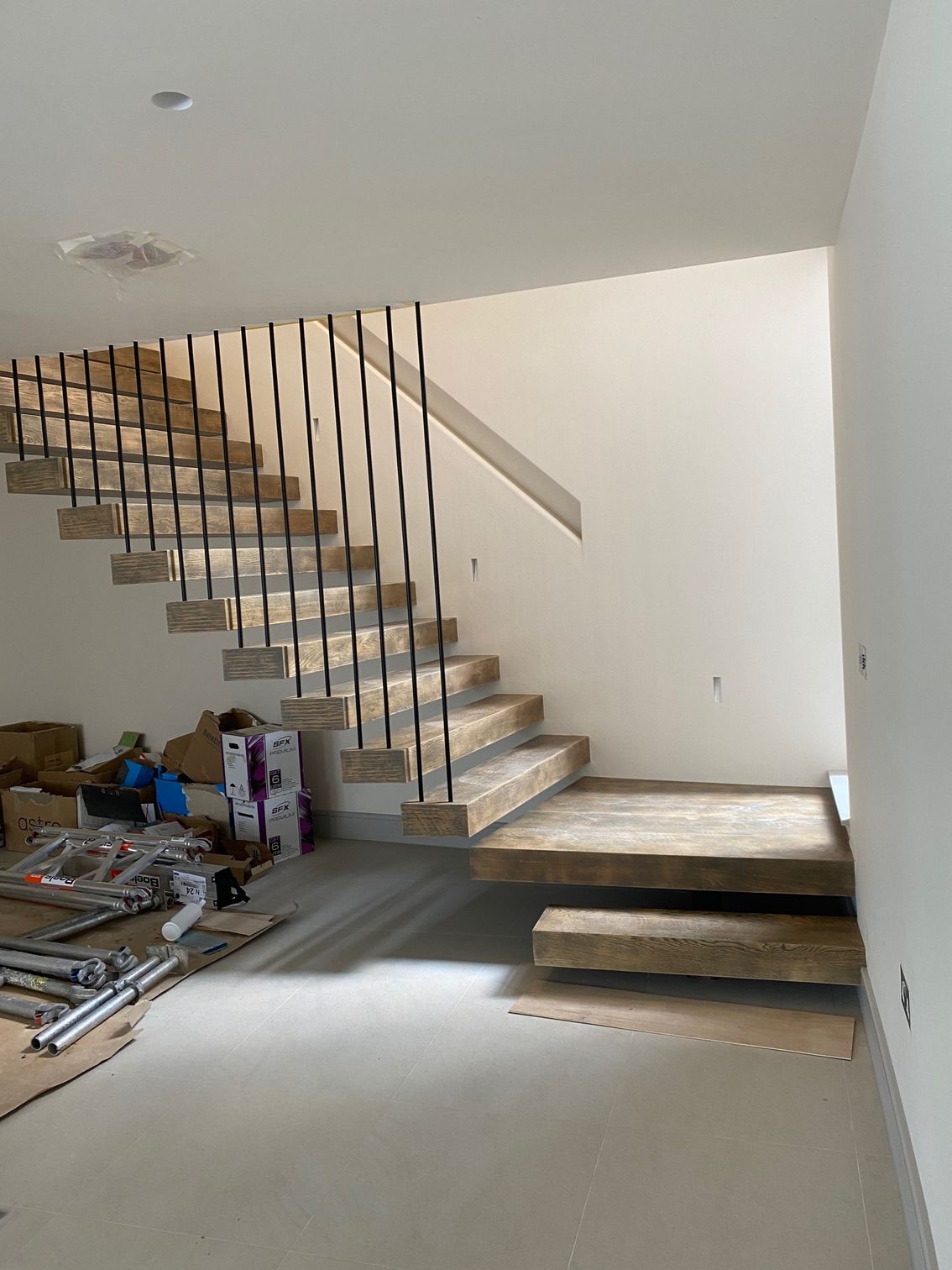 Floating stone stairs with black metal spindles and handrail in an unfinished interior.