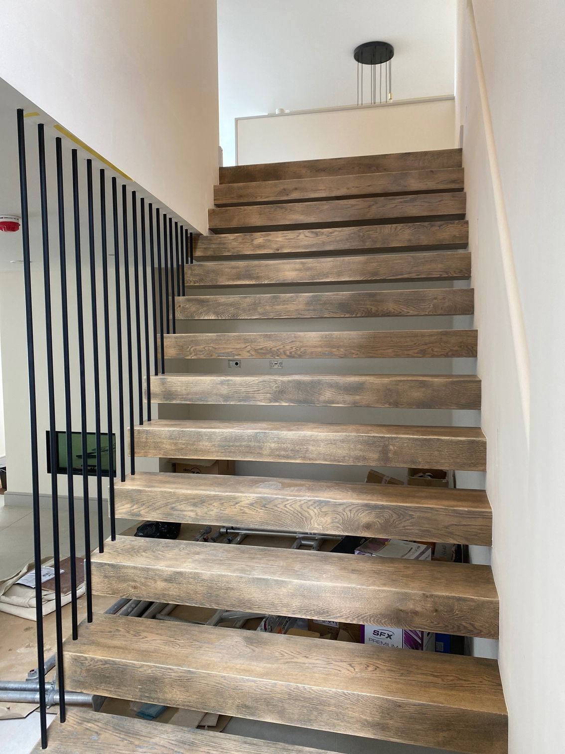 Wooden staircase with black metal railing, leading upwards.