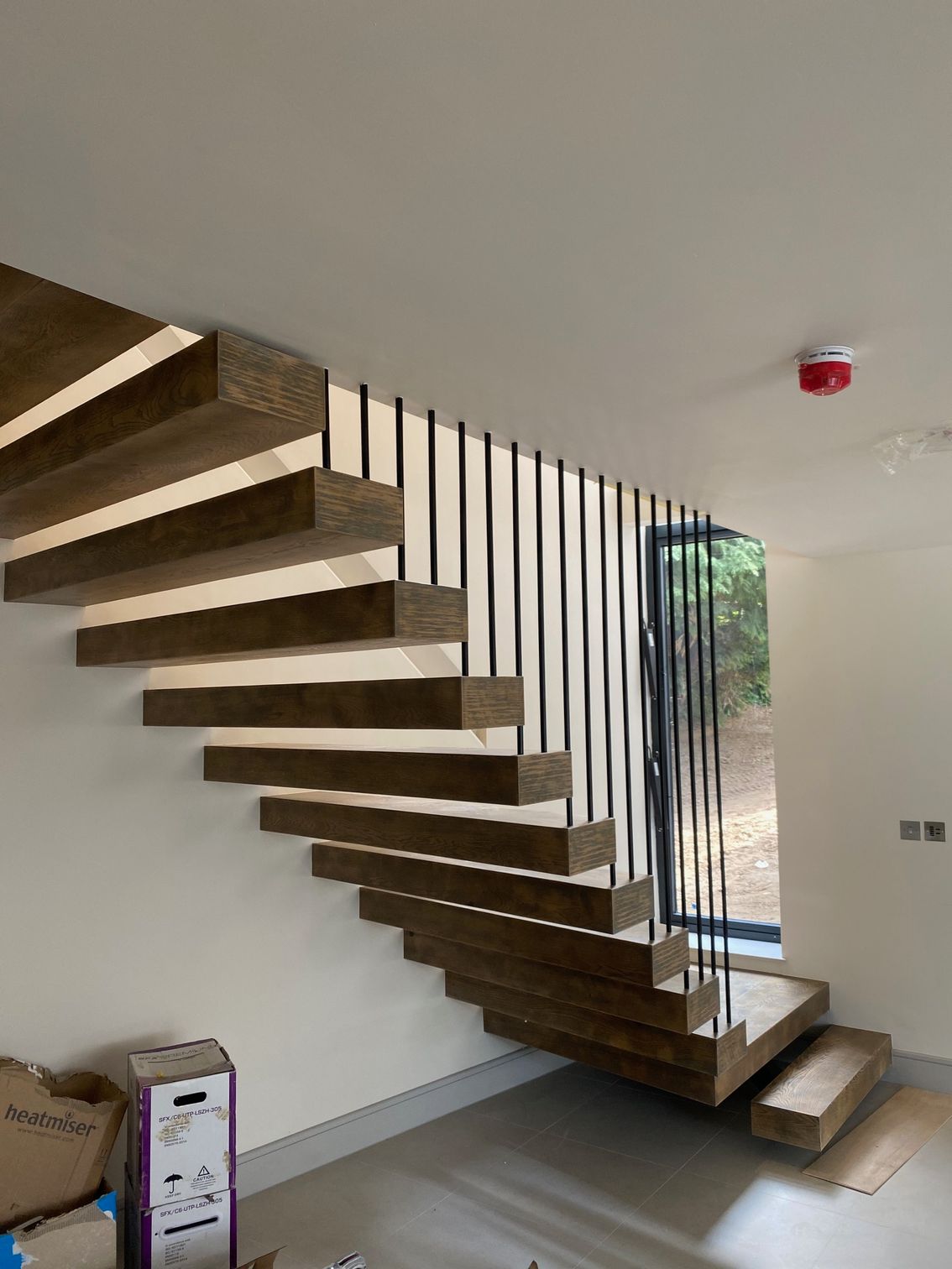 Modern floating wooden staircase with black vertical supports and window.