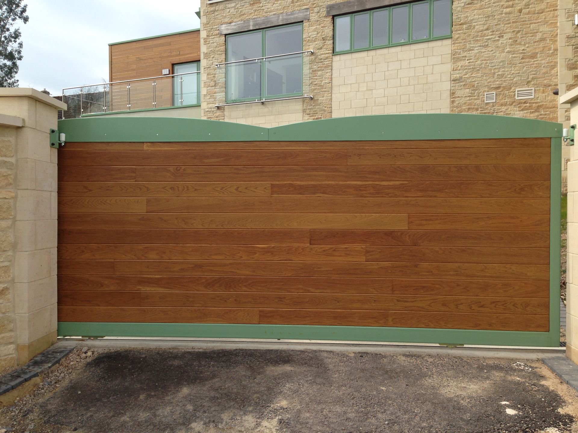Wooden gate with green frame, set in stone pillars, blocking driveway.